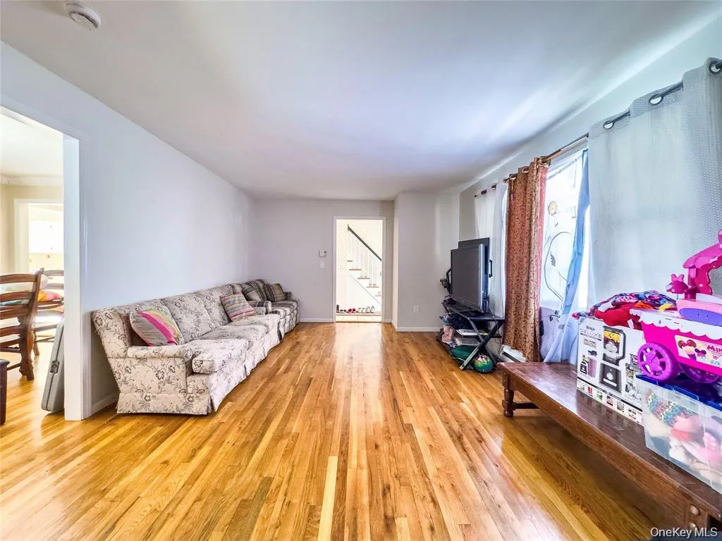 Spacious living area featuring polished wood-finish flooring, light-toned walls, and abundant natural light from multiple windows Spacious living area featuring polished wood-finish flooring, light-toned walls, and abundant natural light from multiple windows