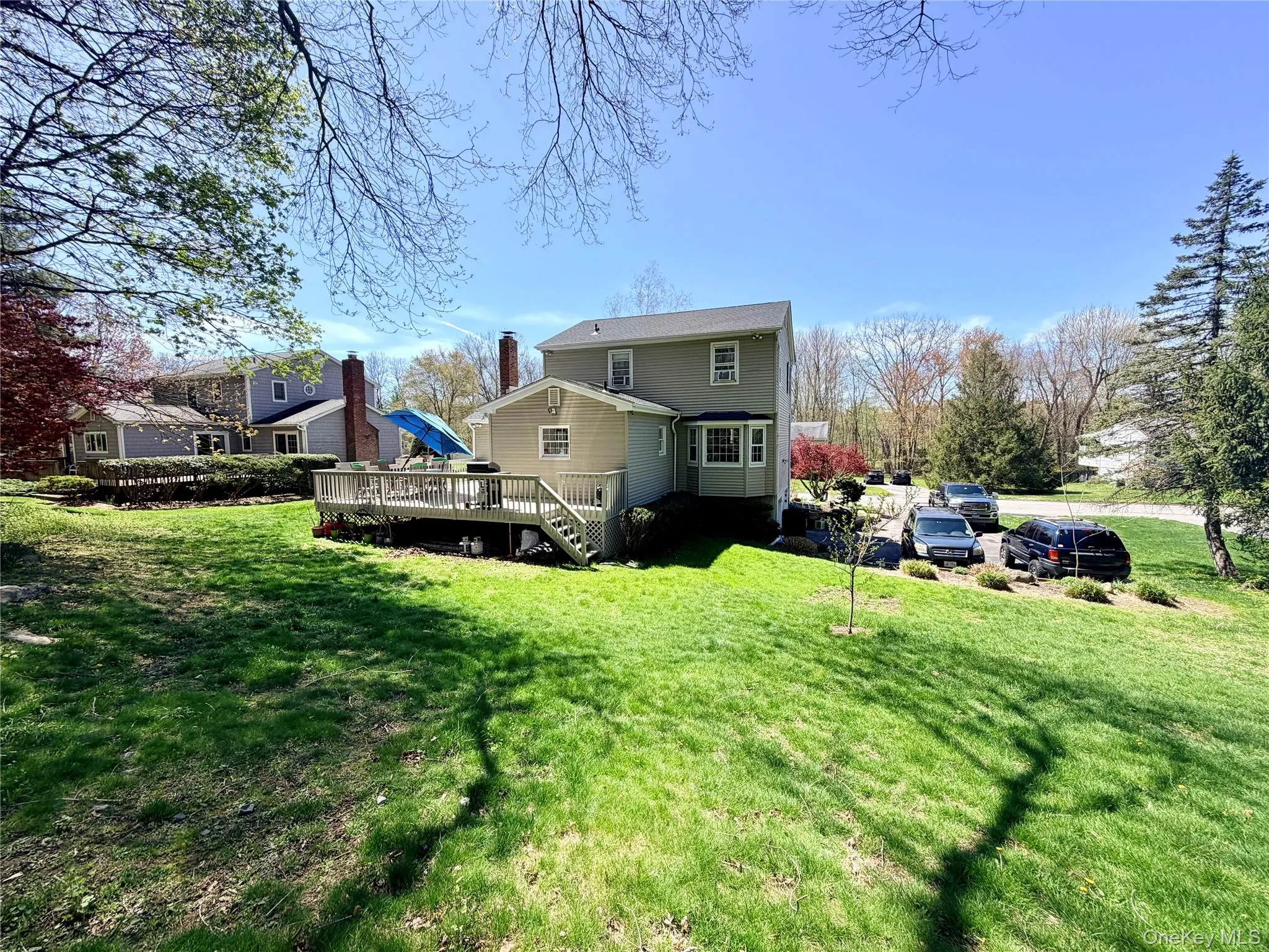 Rear exterior featuring a spacious wood-finish deck with stairs to the lawn, light-colored siding, and a prominent chimney Rear exterior featuring a spacious wood-finish deck with stairs to the lawn, light-colored siding, and a prominent chimney