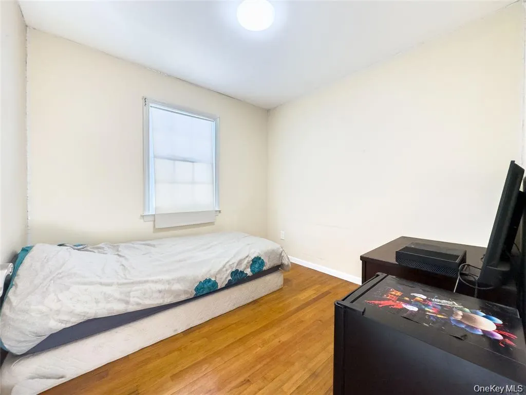 Room featuring wood-finish flooring, a window with a roller shade, and light-toned wall paint Room featuring wood-finish flooring, a window with a roller shade, and light-toned wall paint