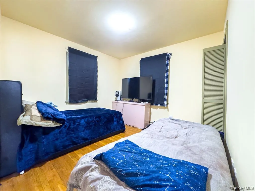 Hardwood flooring throughout, featuring a window with roller shade, and a louvered closet door Hardwood flooring throughout, featuring a window with roller shade, and a louvered closet door