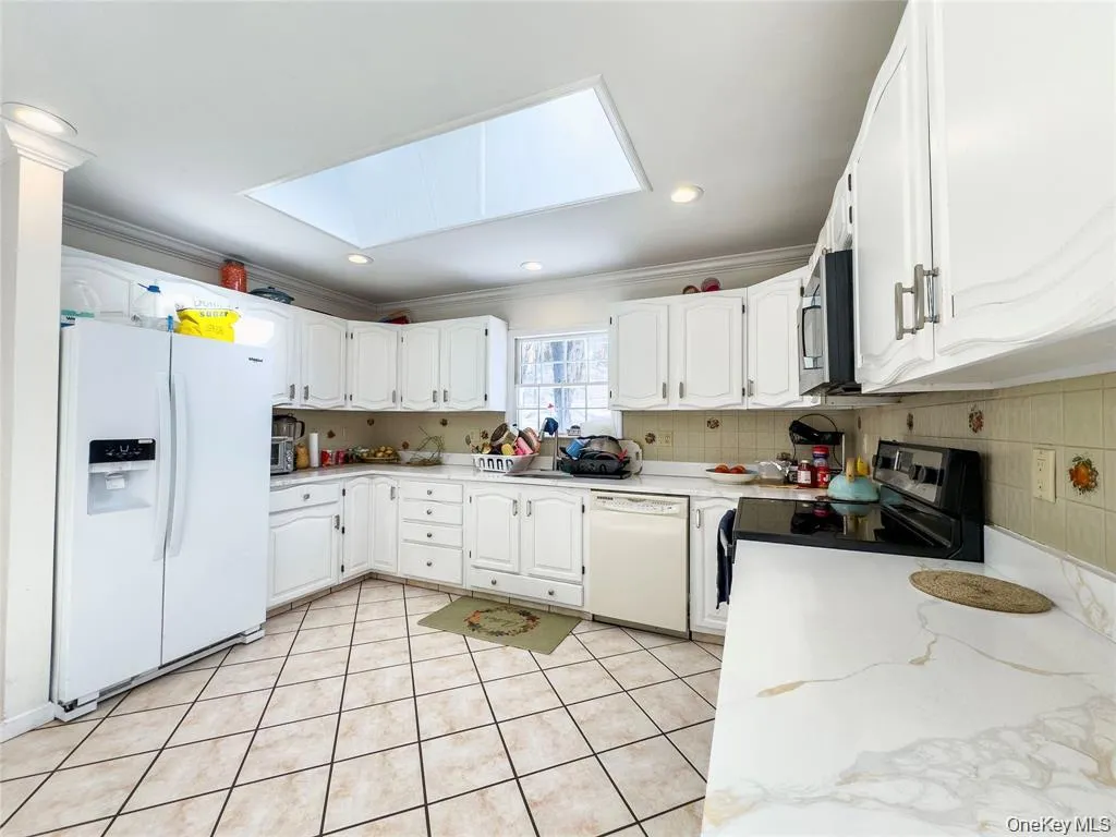 Kitchen featuring a skylight, white cabinetry with silver-tone hardware, a built-in microwave, and a white dishwasher Kitchen featuring a skylight, white cabinetry with silver-tone hardware, a built-in microwave, and a white dishwasher