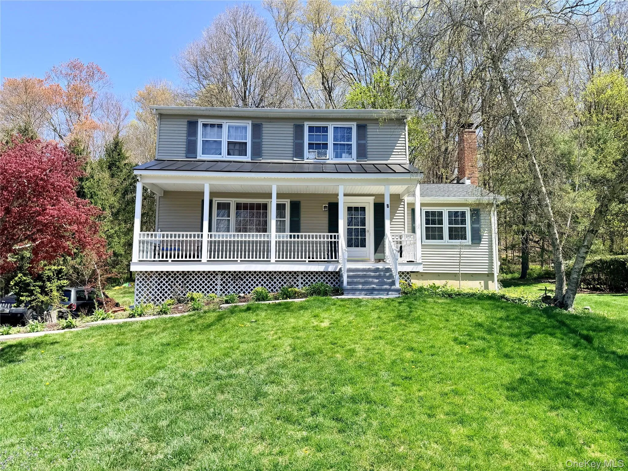 Two-story residence featuring a covered front porch with white railing, light-colored siding, dark shutters, and a prominent brick chimney Two-story residence featuring a covered front porch with white railing, light-colored siding, dark shutters, and a prominent brick chimney