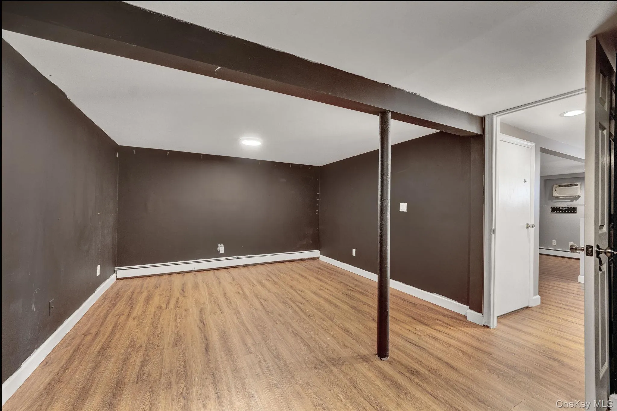 Spacious room featuring wood-finish flooring, dark-painted walls, and white baseboards Spacious room featuring wood-finish flooring, dark-painted walls, and white baseboards