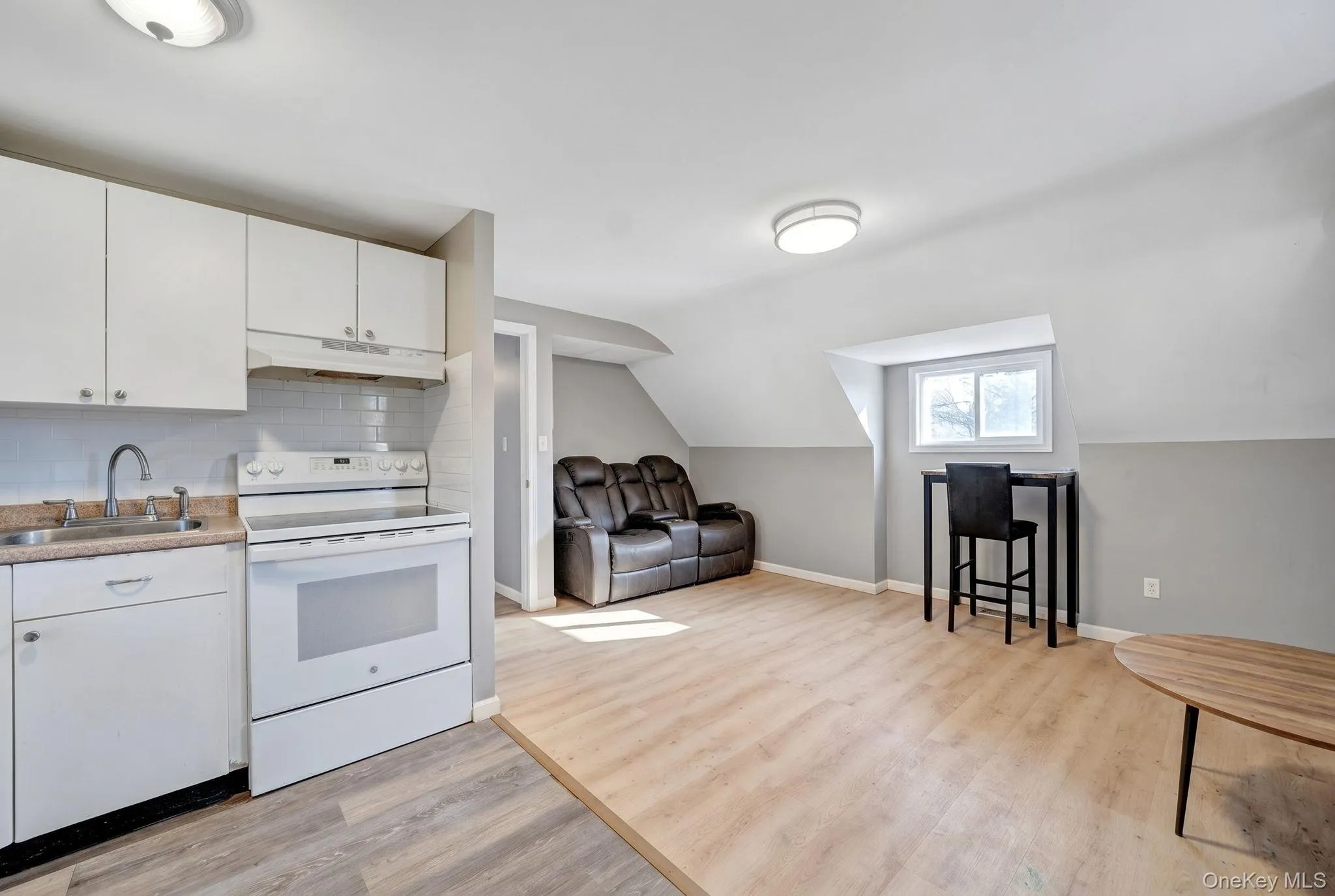 Compact kitchen area featuring white cabinetry, a white electric range, and a subway tile backsplash Compact kitchen area featuring white cabinetry, a white electric range, and a subway tile backsplash