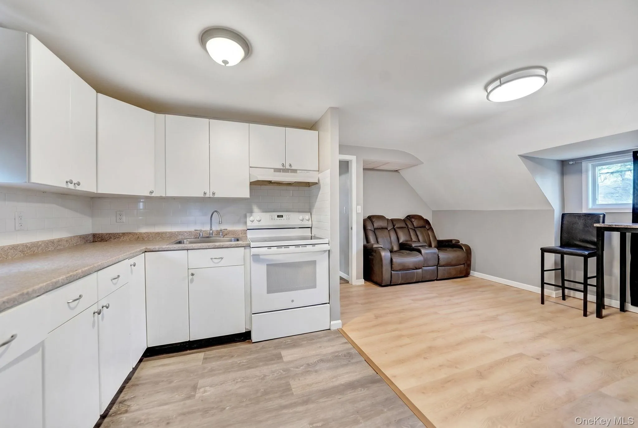 U-shaped kitchen featuring white cabinetry, light-toned countertops, and an included white range2nd floor kitchen and living room U-shaped kitchen featuring white cabinetry, light-toned countertops, and an included white range2nd floor kitchen and living room