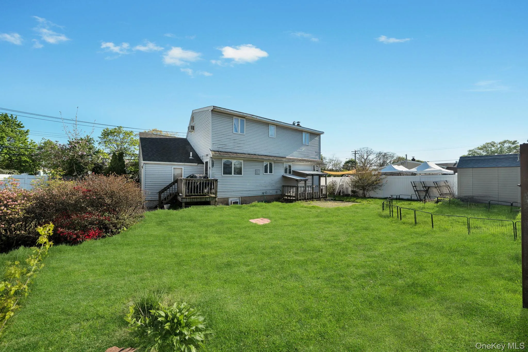 Expansive backyard featuring a manicured lawn, established shrubbery, and a multi-level wood deck Expansive backyard featuring a manicured lawn, established shrubbery, and a multi-level wood deck