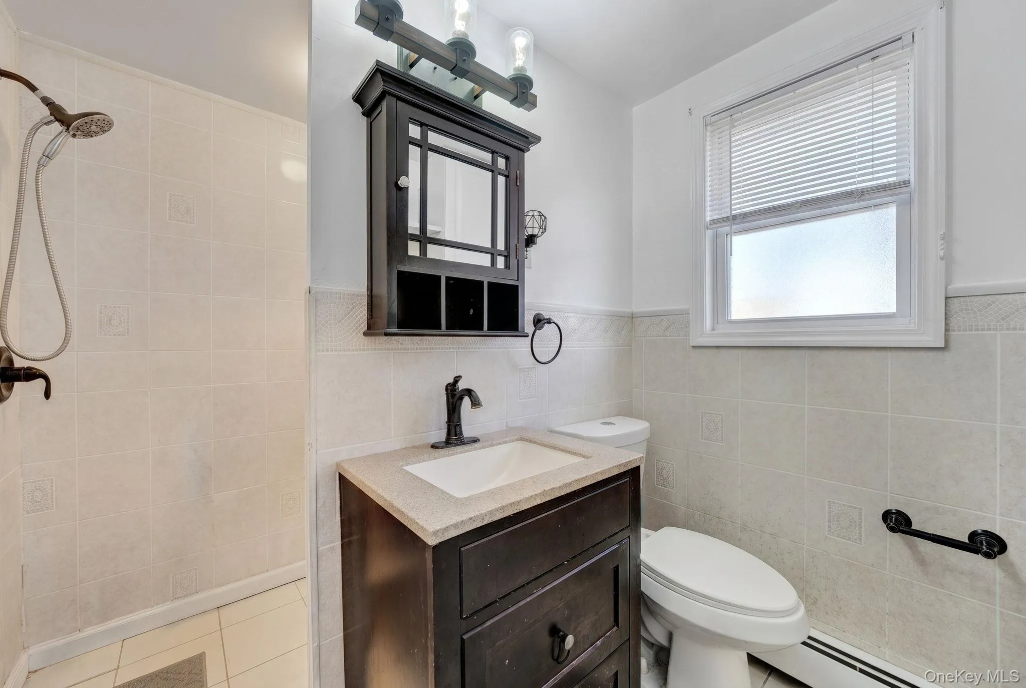 Bathroom featuring a shower with tiled walls, a dark wood-finish vanity with a light-toned countertop and integrated sink, a dark wood-finish medicine cabinet with a mirror, and a window with blinds 2nd floor bathroom Bathroom featuring a shower with tiled walls, a dark wood-finish vanity with a light-toned countertop and integrated sink, a dark wood-finish medicine cabinet with a mirror, and a window with blinds 2nd floor bathroom