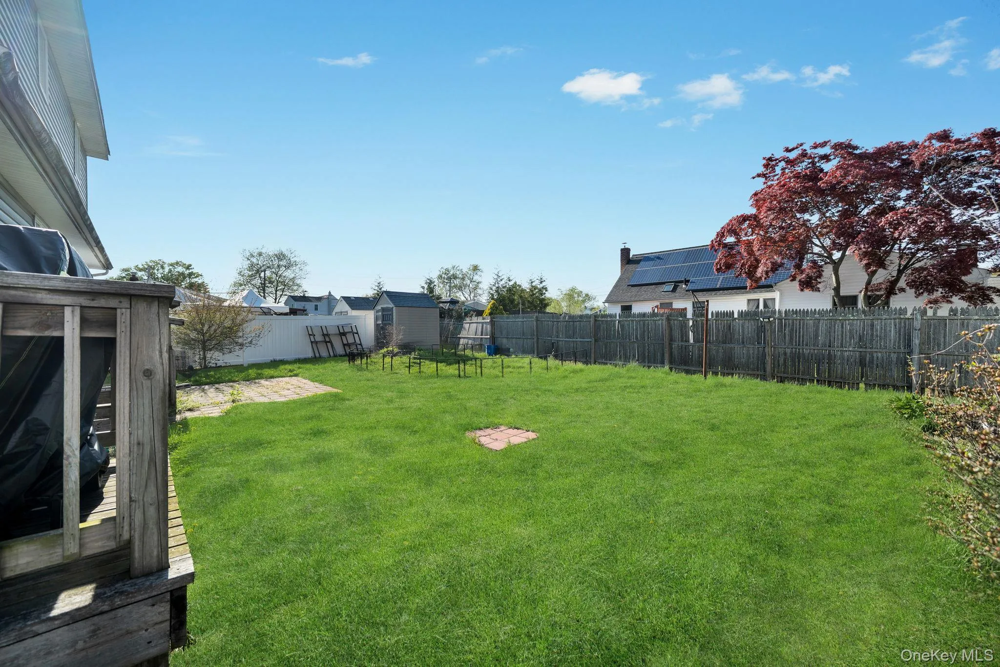 Expansive green lawn with a privacy fence, mature trees, and a wooden deck Expansive green lawn with a privacy fence, mature trees, and a wooden deck