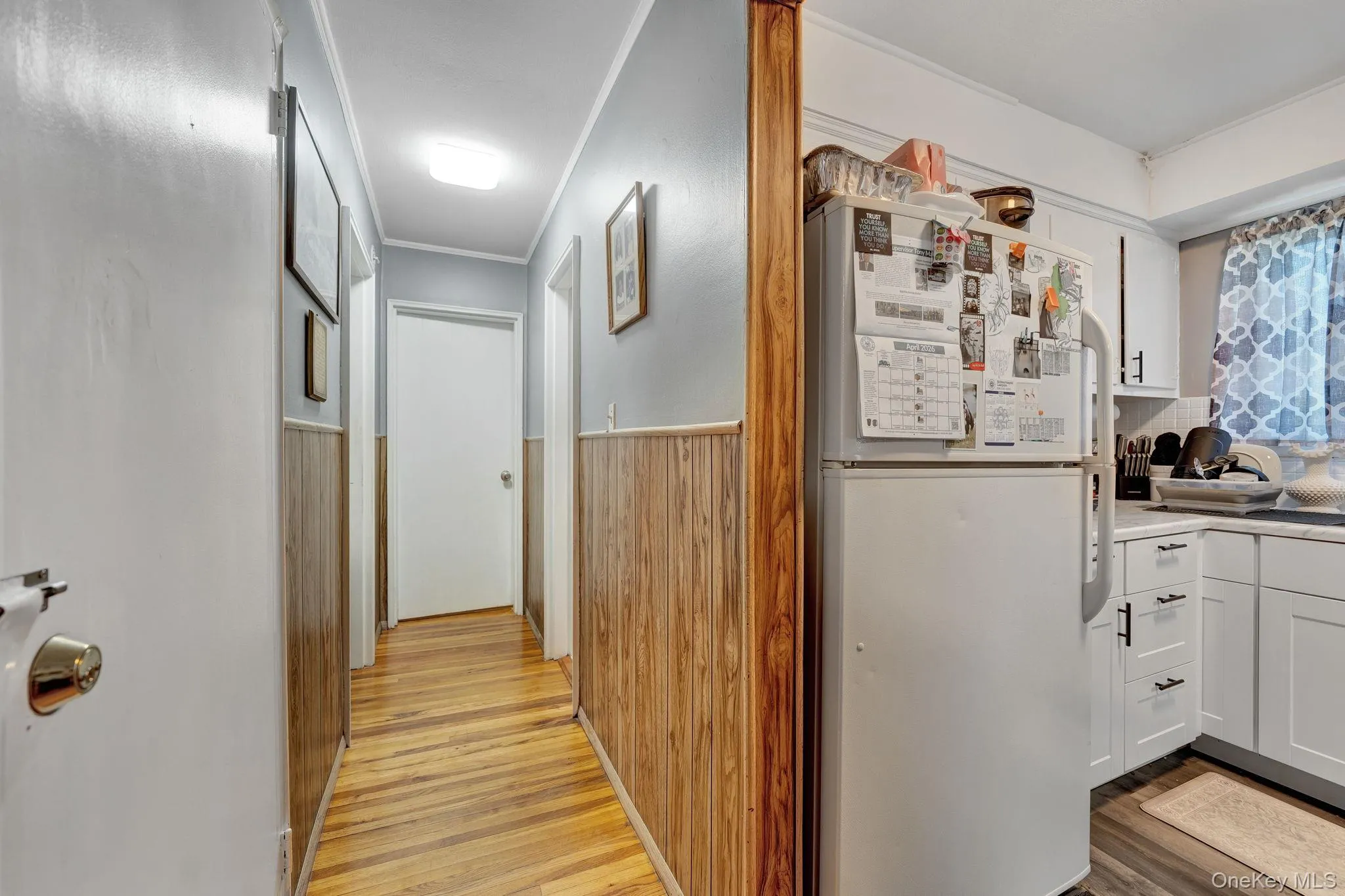 Hallway with wood-finish flooring and wainscoting, featuring multiple white doors Hallway with wood-finish flooring and wainscoting, featuring multiple white doors