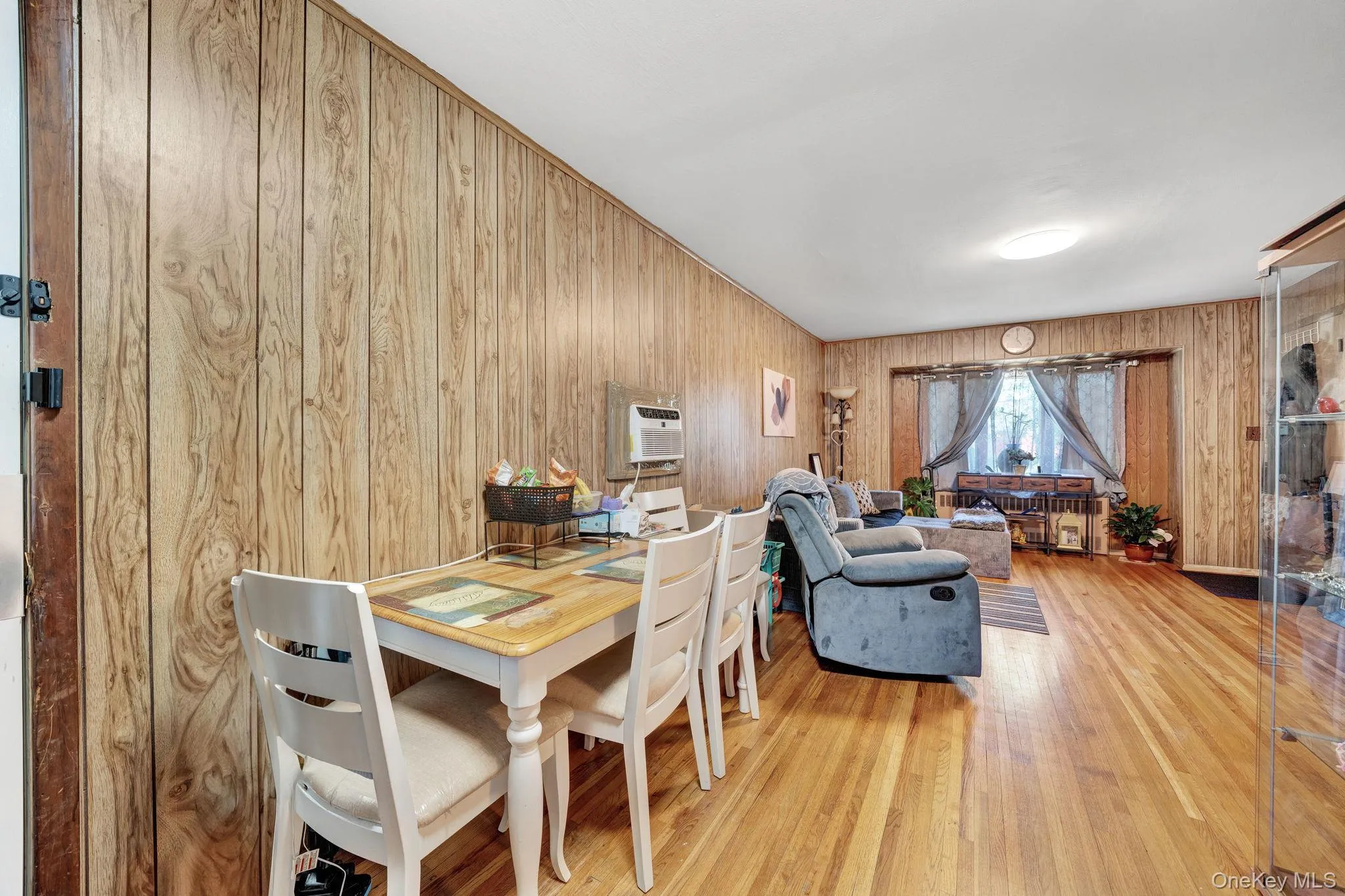 Open-concept living space featuring wood-finish paneling, hardwood flooring, and a large window with natural light 1st floor dining and living Open-concept living space featuring wood-finish paneling, hardwood flooring, and a large window with natural light 1st floor dining and living