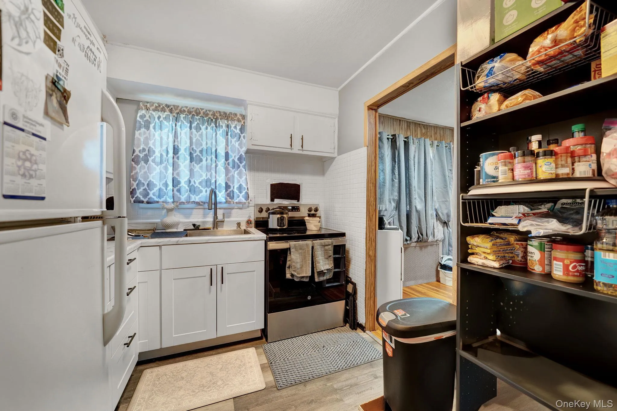 Kitchen featuring white shaker-style cabinetry, a stainless steel sink with a gooseneck faucet, a white tile backsplash, and wood-finish flooring Kitchen featuring white shaker-style cabinetry, a stainless steel sink with a gooseneck faucet, a white tile backsplash, and wood-finish flooring