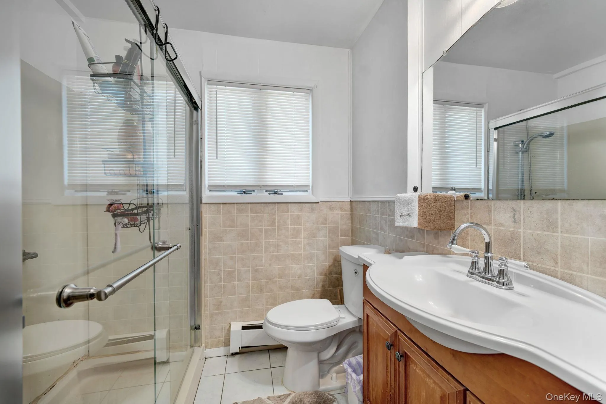 Bathroom featuring a glass-enclosed shower, a vanity with a white integrated sink, a large mirror, and tiled walls 1st floor Bathroom featuring a glass-enclosed shower, a vanity with a white integrated sink, a large mirror, and tiled walls 1st floor