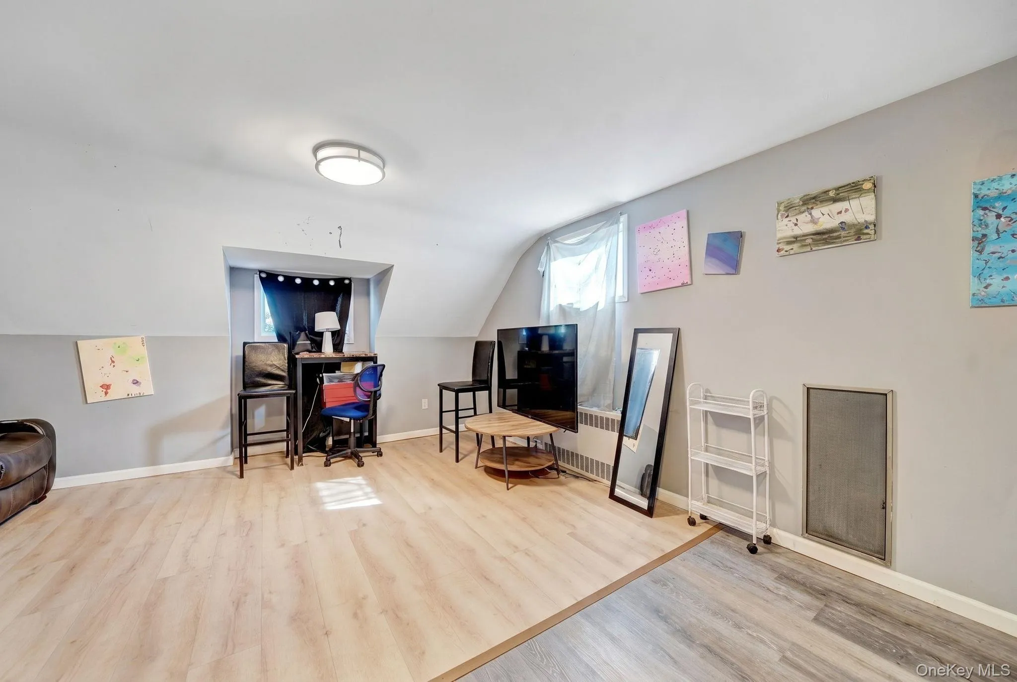 Room featuring light wood-finish flooring, two-tone gray and white walls, an angled ceiling line, and a flush-mount ceiling light fixture Room featuring light wood-finish flooring, two-tone gray and white walls, an angled ceiling line, and a flush-mount ceiling light fixture