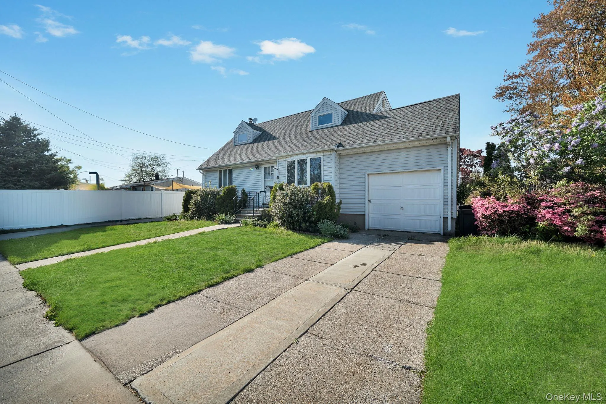 Light blue siding exterior featuring a multi-pane bay window, two dormer windows, a single-car garage, and a concrete driveway Light blue siding exterior featuring a multi-pane bay window, two dormer windows, a single-car garage, and a concrete driveway