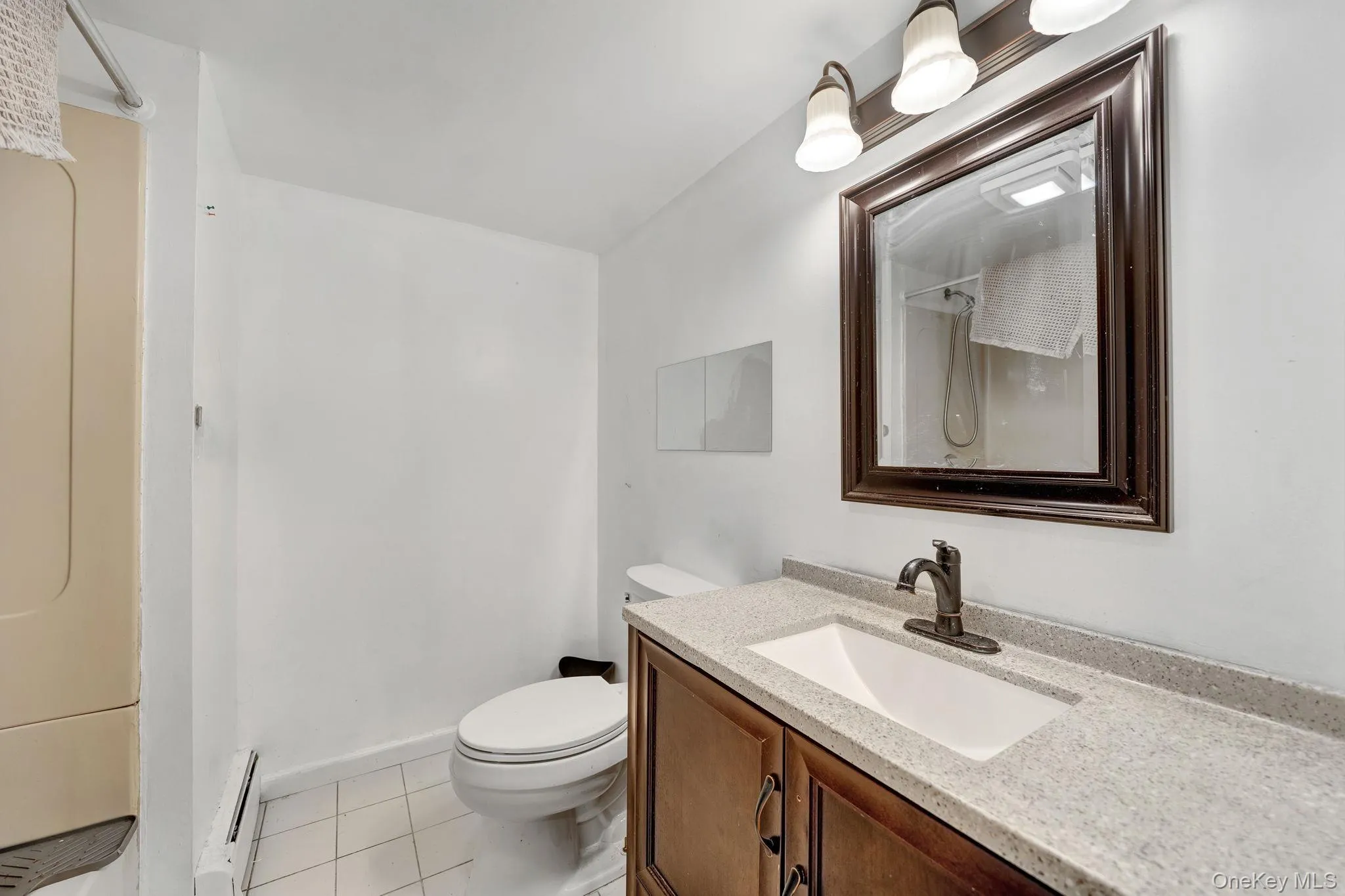 Bathroom vanity featuring a light-colored countertop with an integrated sink, dark wood-finish cabinetry, and a dark-framed mirrorbasement bathroom Bathroom vanity featuring a light-colored countertop with an integrated sink, dark wood-finish cabinetry, and a dark-framed mirrorbasement bathroom
