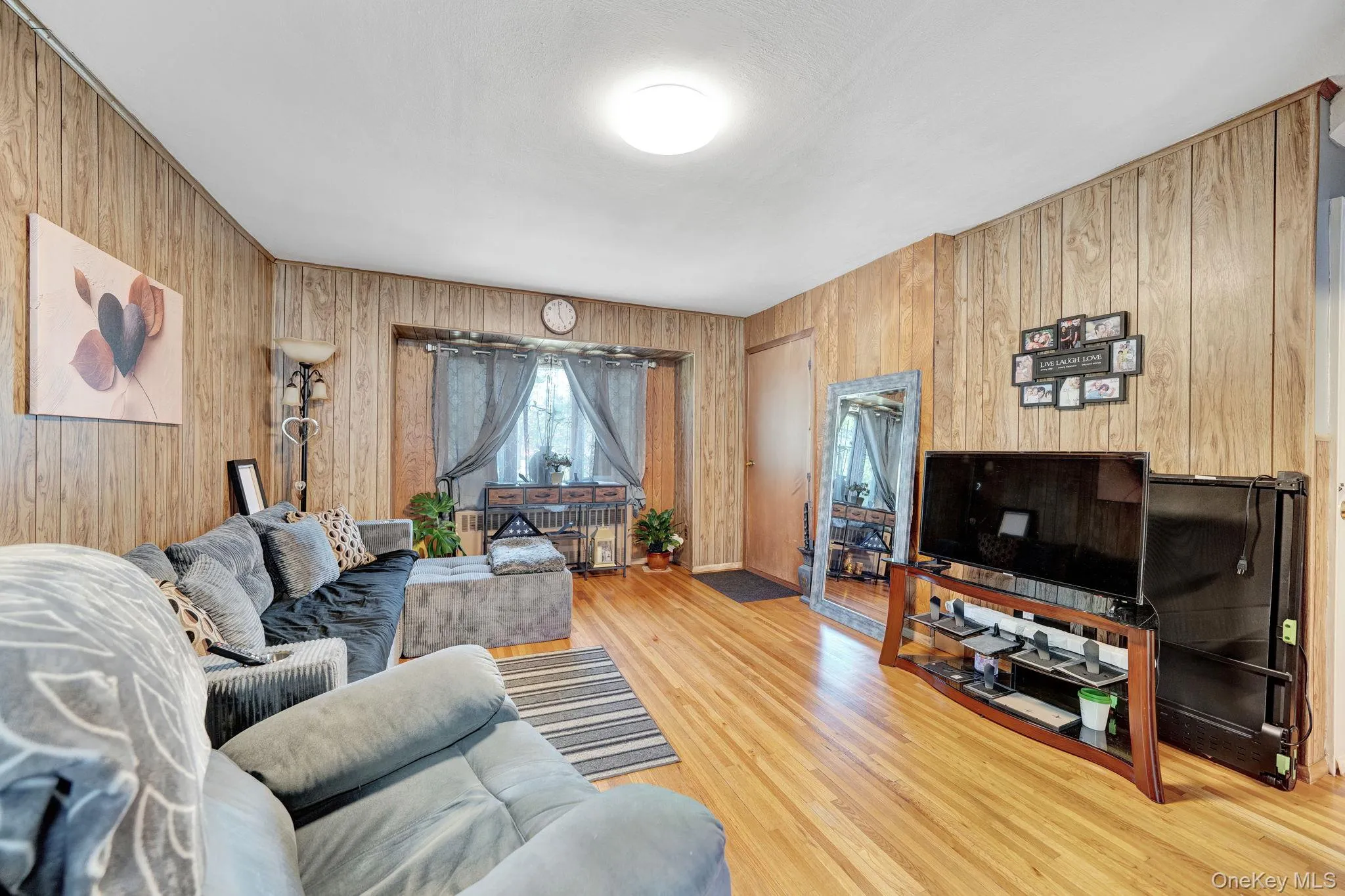 Living area featuring wood-finish wall paneling, hardwood flooring, and a flush-mount ceiling light fixture Living area featuring wood-finish wall paneling, hardwood flooring, and a flush-mount ceiling light fixture