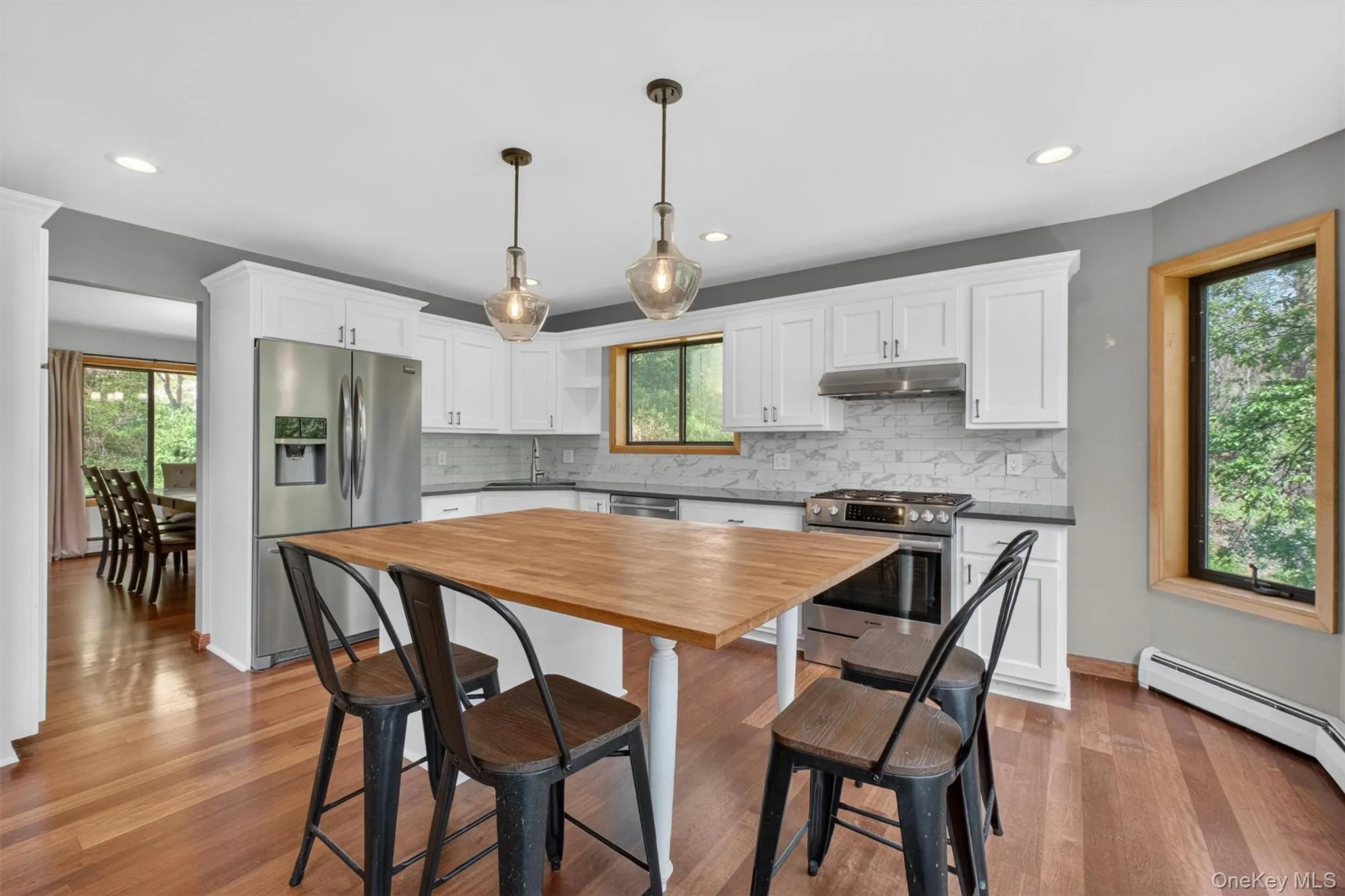 Kitchen featuring white cabinetry, dark countertops, a subway tile backsplash, stainless steel appliances, butcher block island, wood-finish flooring, leading out to the dining room. Kitchen featuring white cabinetry, dark countertops, a subway tile backsplash, stainless steel appliances, butcher block island, wood-finish flooring, leading out to the dining room.