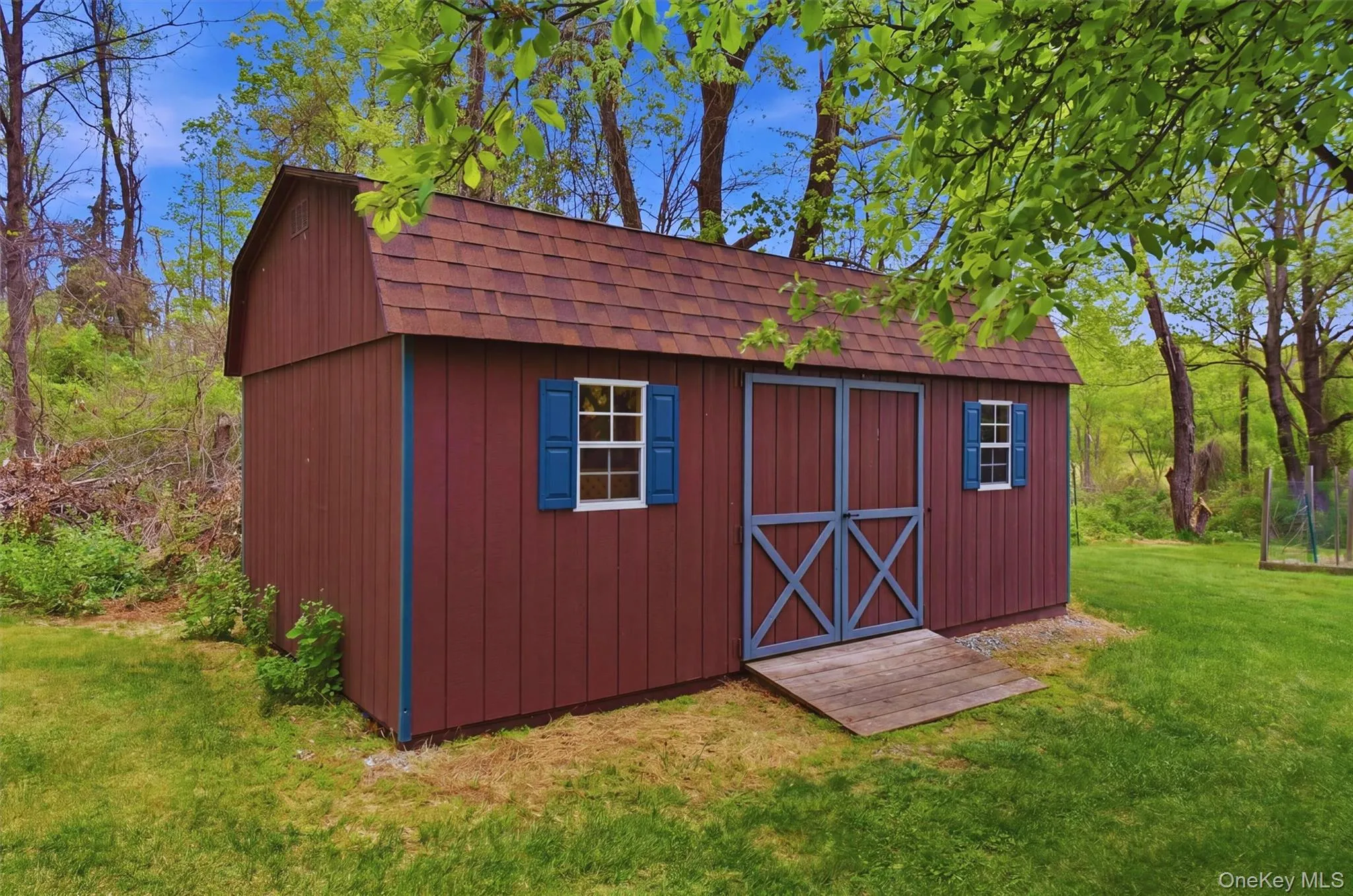 Gable-roofed shed with brown siding and a shingle roof in back of property. Gable-roofed shed with brown siding and a shingle roof in back of property.