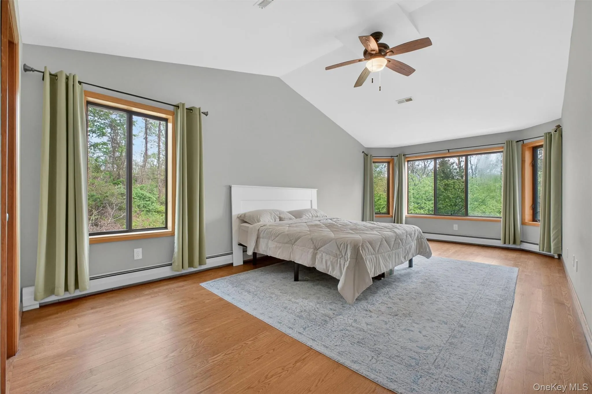 Spacious vaulted ceiling bedroom featuring wood-finish flooring, a ceiling fan, and multiple windows with wood trim Spacious vaulted ceiling bedroom featuring wood-finish flooring, a ceiling fan, and multiple windows with wood trim