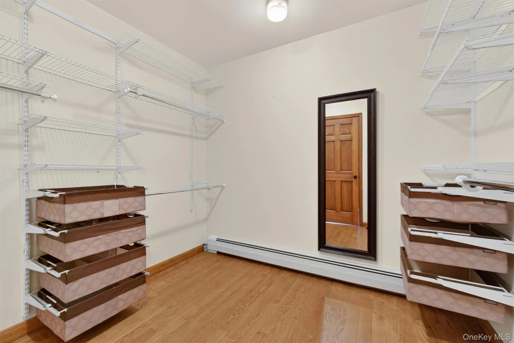 Walk-in closet featuring light wood-finish flooring, adjustable wire shelving systems, and a wall-mounted full-length mirror Walk-in closet featuring light wood-finish flooring, adjustable wire shelving systems, and a wall-mounted full-length mirror