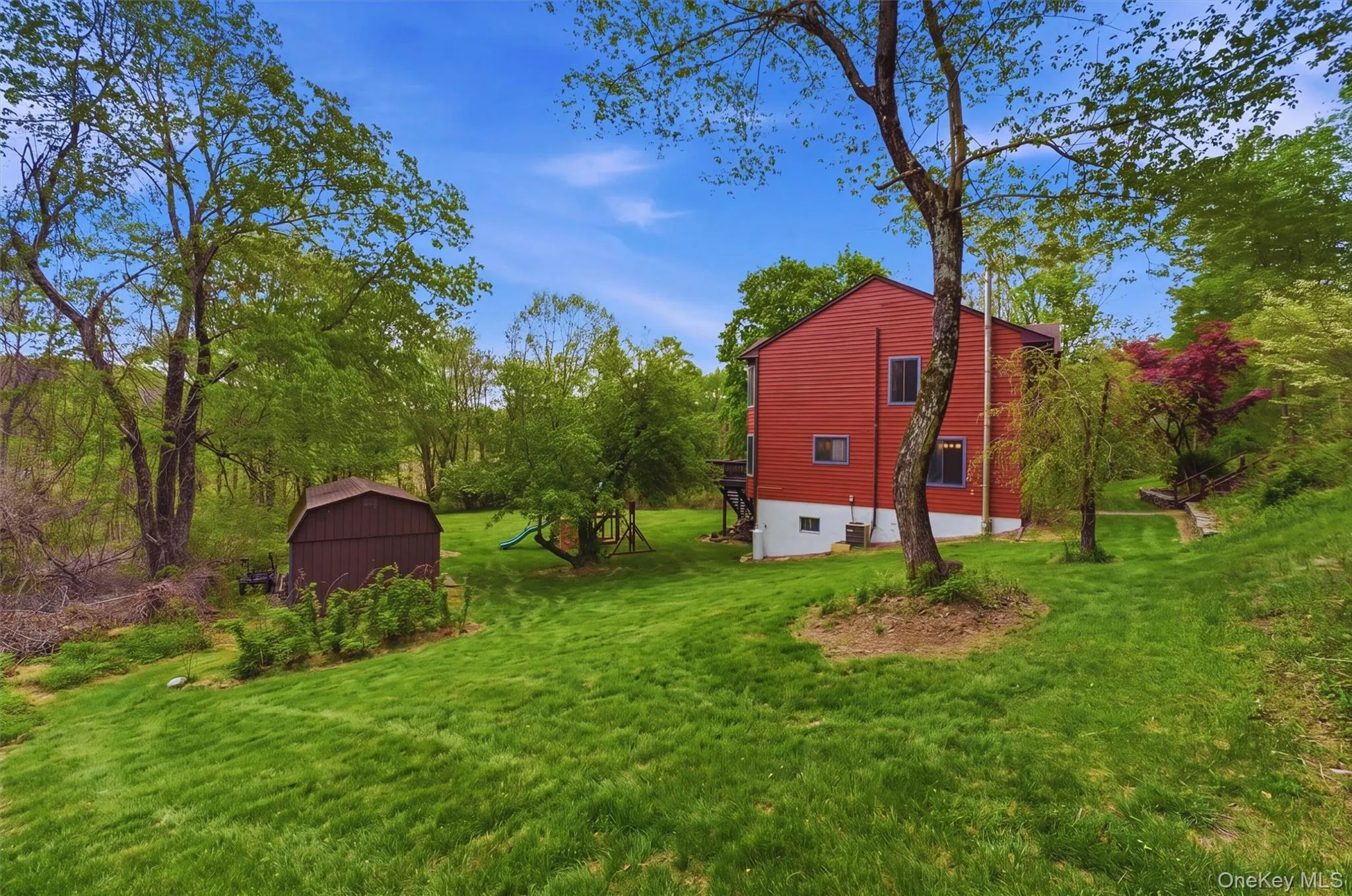 Expansive green lawn surrounds a red contemporary home with a shed and garden. Expansive green lawn surrounds a red contemporary home with a shed and garden.