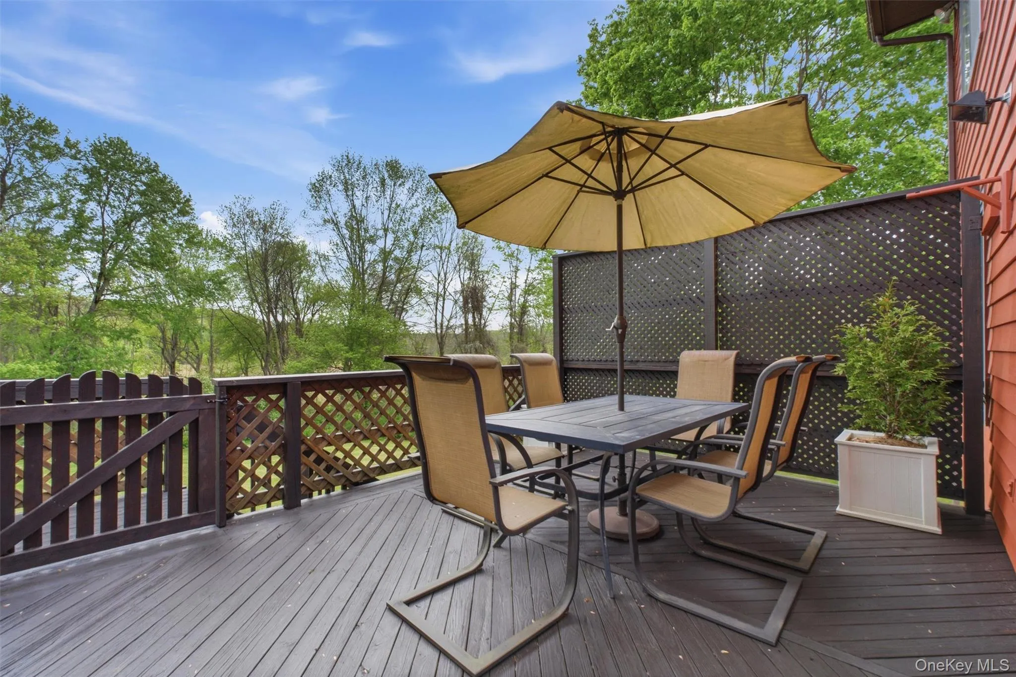 Expansive wood deck with a privacy lattice wall, offering direct access to the interior via a large sliding glass door, overlooking the lawn. Expansive wood deck with a privacy lattice wall, offering direct access to the interior via a large sliding glass door, overlooking the lawn.