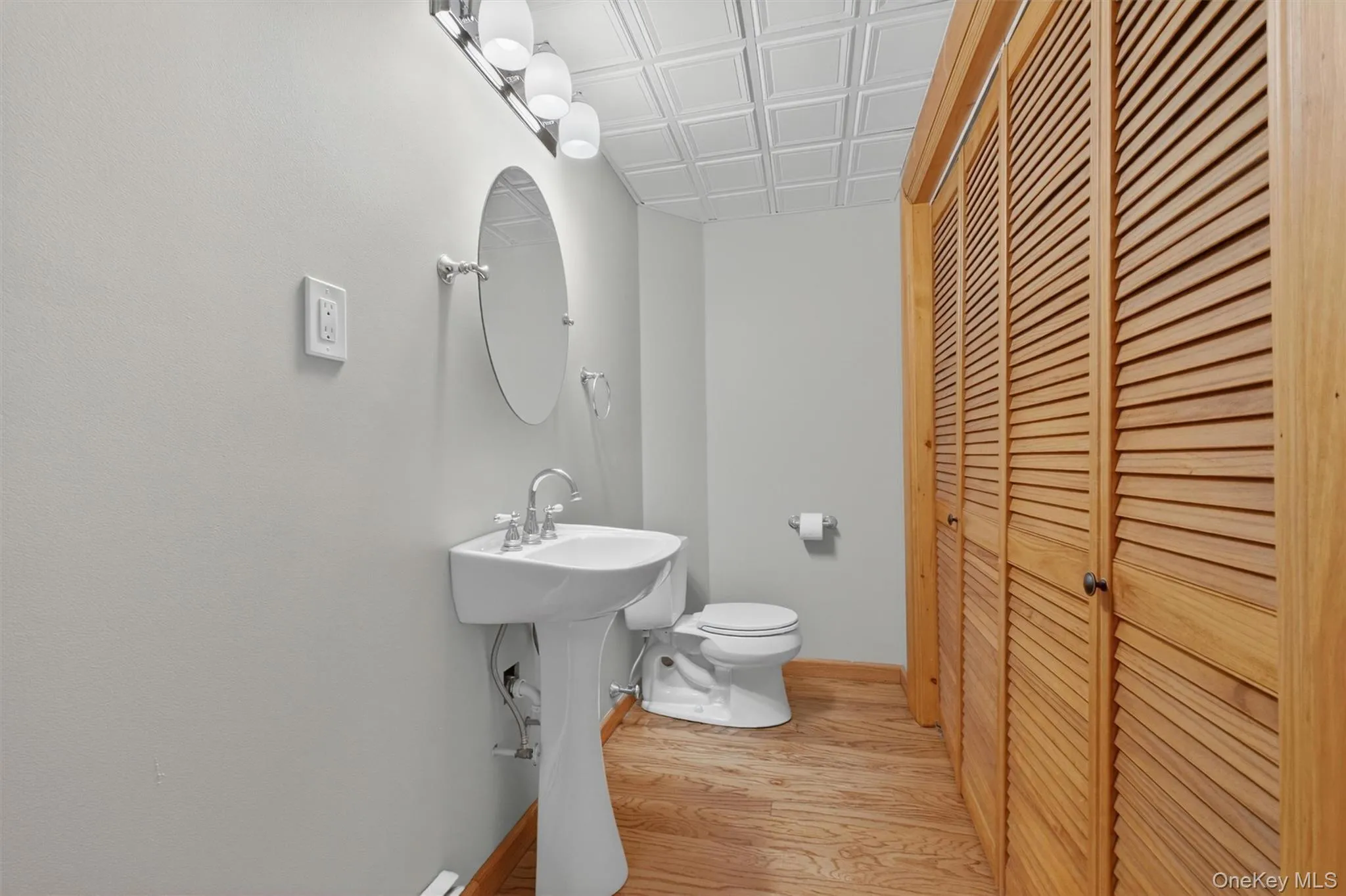 Bathroom featuring a pedestal sink, oval mirror, and a three-bulb vanity light fixture. Bathroom featuring a pedestal sink, oval mirror, and a three-bulb vanity light fixture.