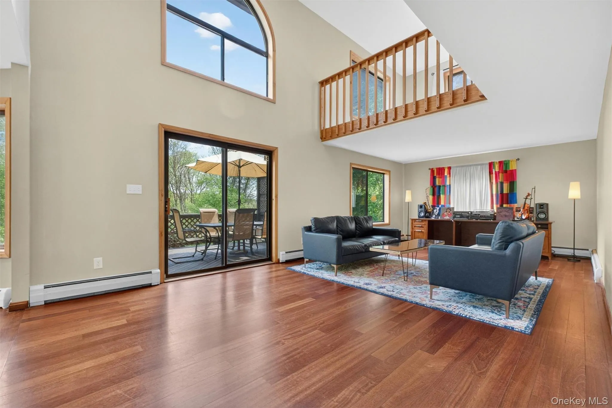 Spacious and bright interior featuring high ceilings, wood-finish flooring, and a sliding glass door providing outdoor access to a deck. Spacious and bright interior featuring high ceilings, wood-finish flooring, and a sliding glass door providing outdoor access to a deck.