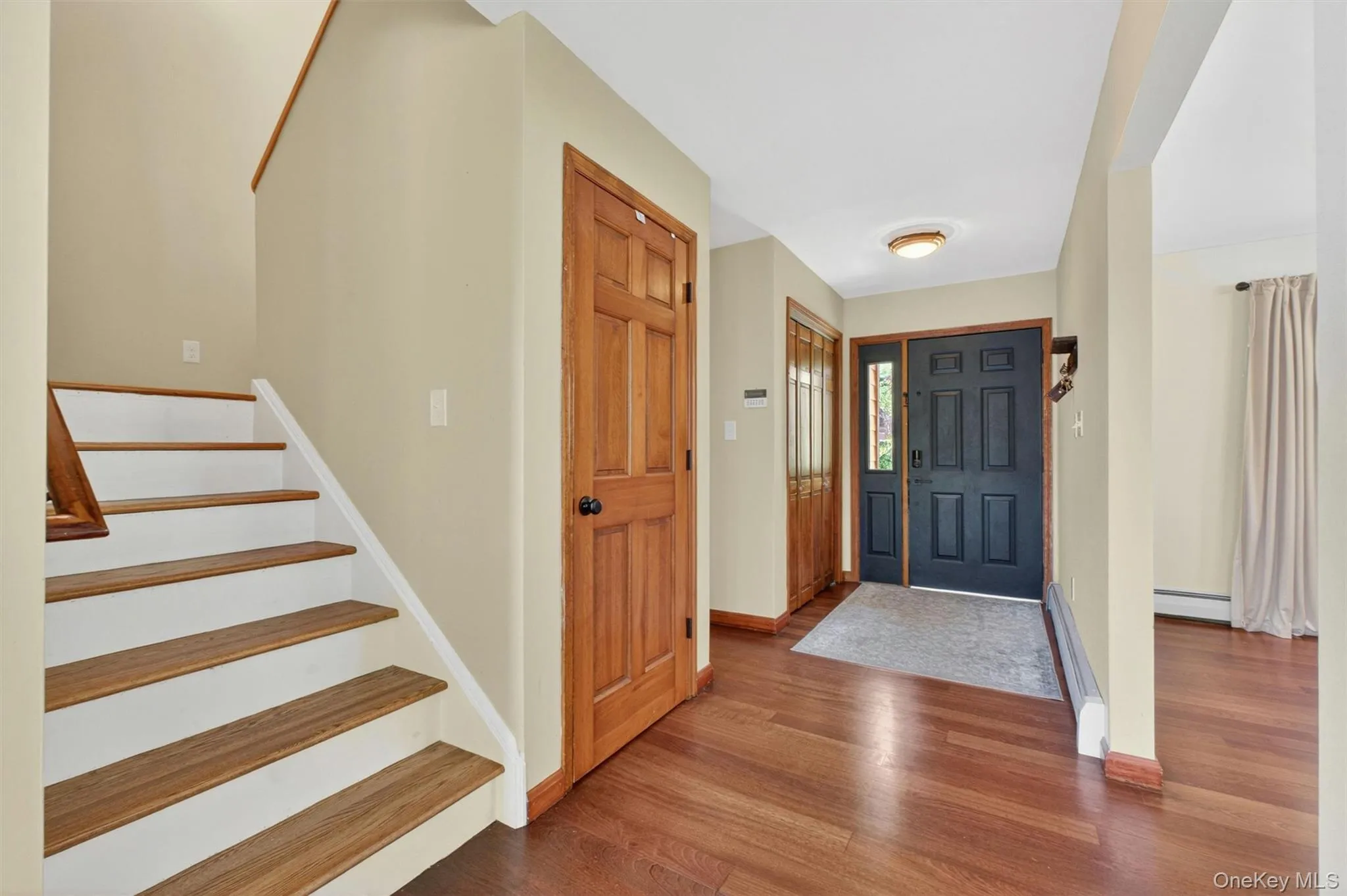 Entry foyer with wood-finish flooring, a dark-paneled entry door with sidelight, and a staircase featuring wood treads and white risers leading upstairs. Entry foyer with wood-finish flooring, a dark-paneled entry door with sidelight, and a staircase featuring wood treads and white risers leading upstairs.