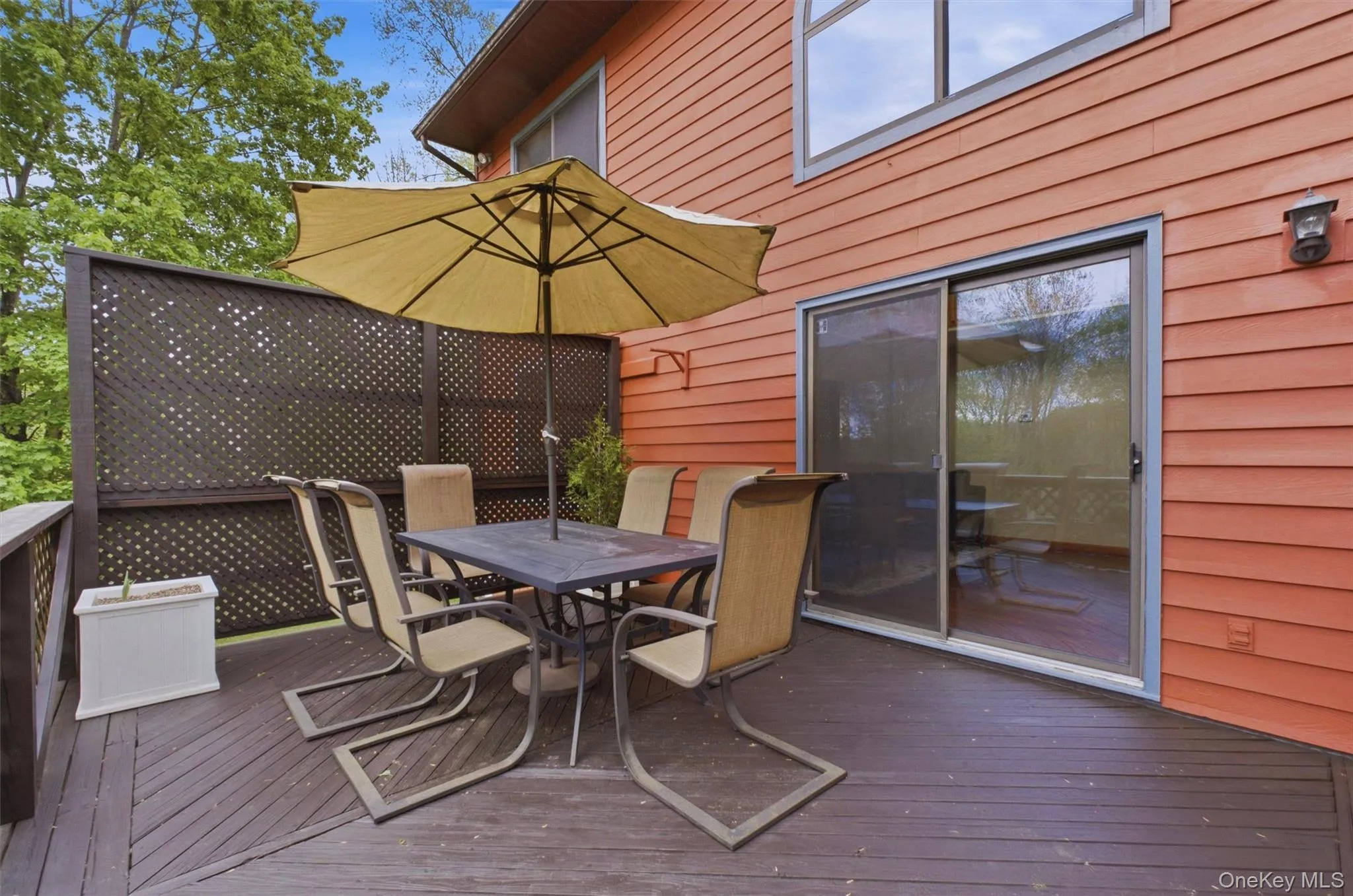 Expansive wood deck with a privacy lattice wall, offering direct access to the interior via a large sliding glass door, overlooking the lawn. Expansive wood deck with a privacy lattice wall, offering direct access to the interior via a large sliding glass door, overlooking the lawn.