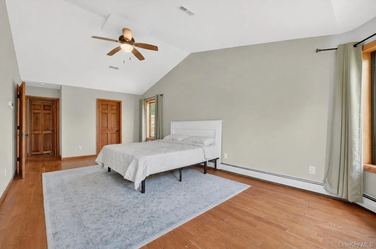 Spacious vaulted ceiling bedroom featuring wood-finish flooring, a ceiling fan, and multiple windows with wood trim Spacious vaulted ceiling bedroom featuring wood-finish flooring, a ceiling fan, and multiple windows with wood trim
