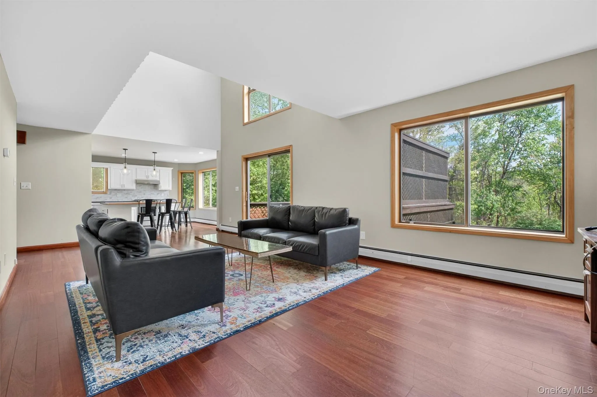 Spacious and bright interior featuring high ceilings, wood-finish flooring, and a sliding glass door providing outdoor access to a deck. Spacious and bright interior featuring high ceilings, wood-finish flooring, and a sliding glass door providing outdoor access to a deck.