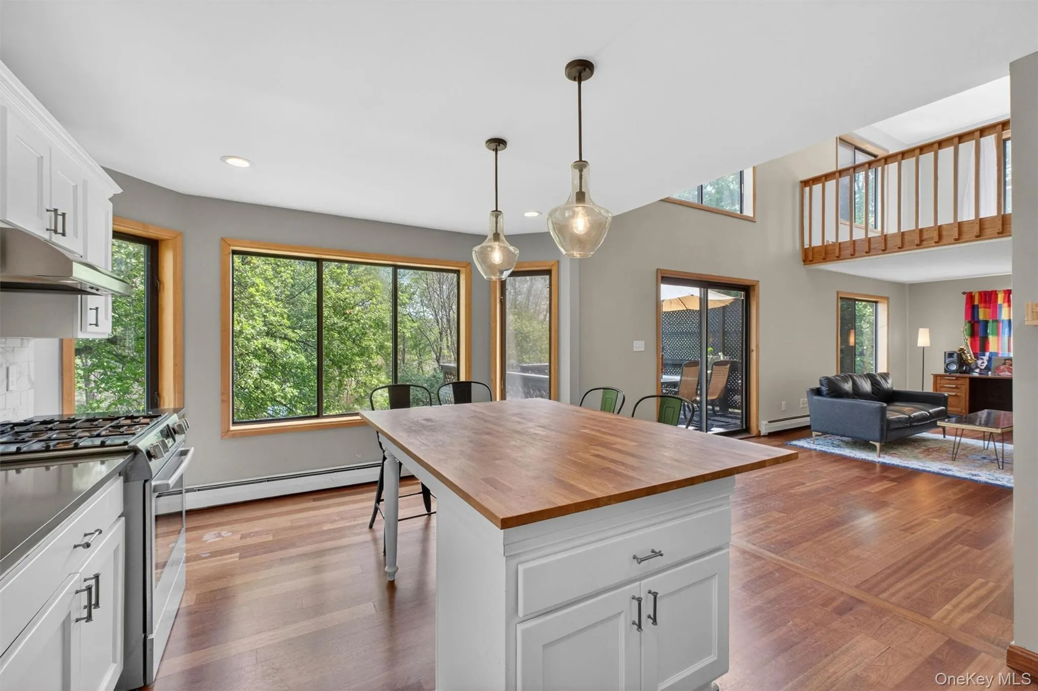 Open concept kitchen to the living room, featuring white cabinetry, dark countertops, a subway tile backsplash, stainless steel appliances, butcher block island, wood-finish flooring and a view of the outdoors. Open concept kitchen to the living room, featuring white cabinetry, dark countertops, a subway tile backsplash, stainless steel appliances, butcher block island, wood-finish flooring and a view of the outdoors.