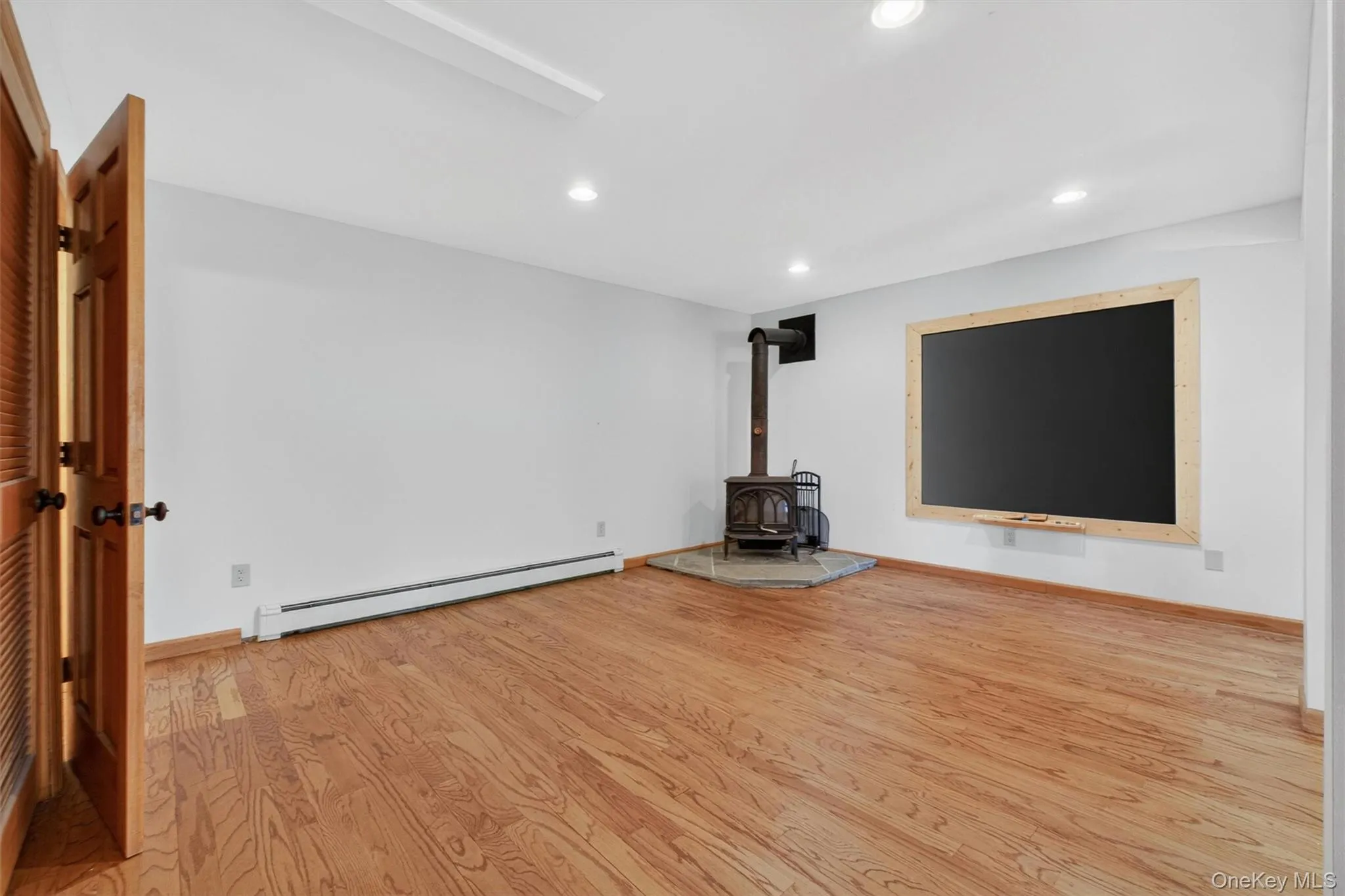 Spacious basement featuring wood-finish flooring, recessed lighting, and a prominent wood-burning stove with a stone surrounding. Spacious basement featuring wood-finish flooring, recessed lighting, and a prominent wood-burning stove with a stone surrounding.