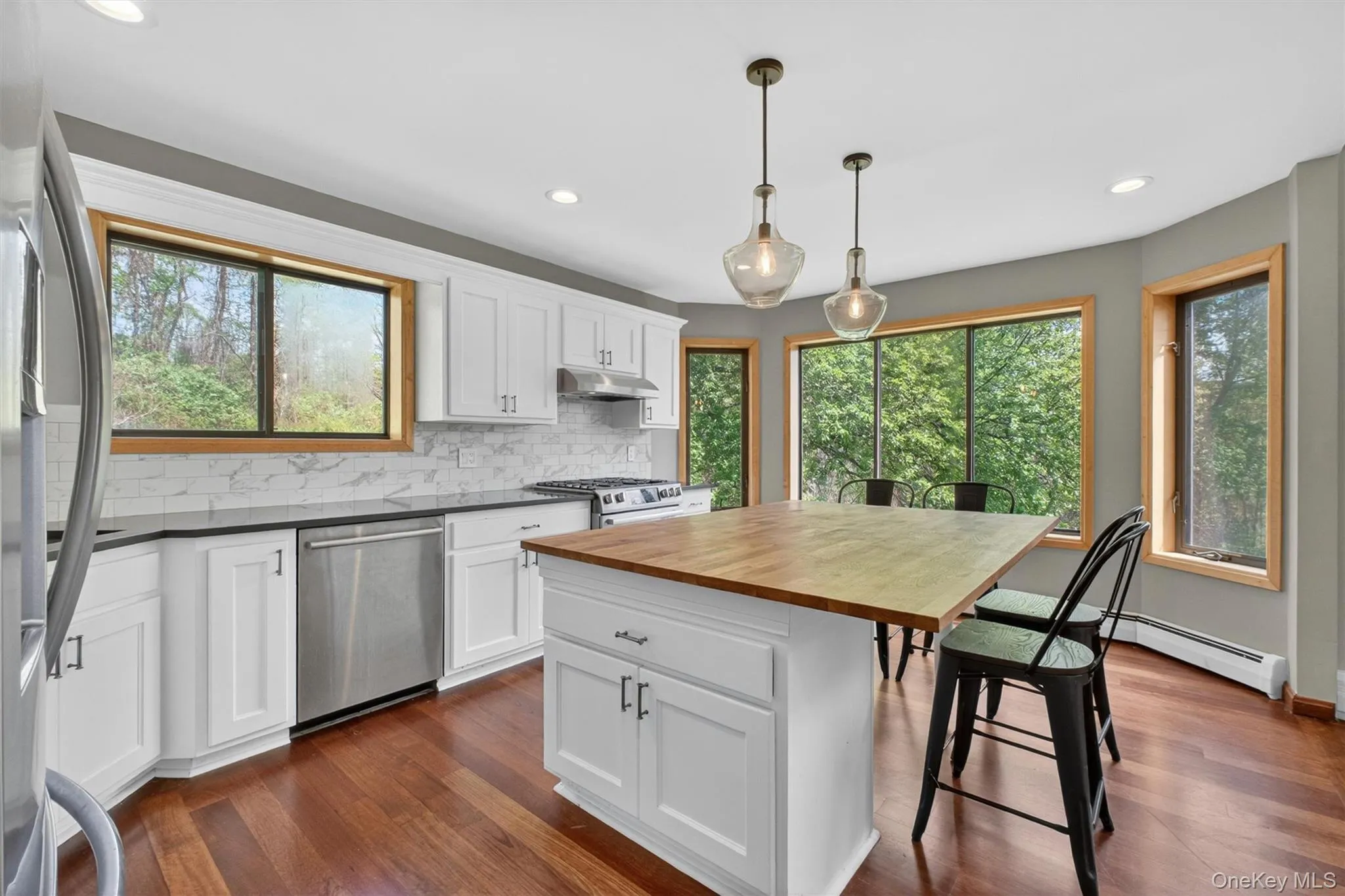 Kitchen featuring white cabinetry, dark countertops, a subway tile backsplash, stainless steel appliances, butcher block island, and wood-finish flooring Kitchen featuring white cabinetry, dark countertops, a subway tile backsplash, stainless steel appliances, butcher block island, and wood-finish flooring