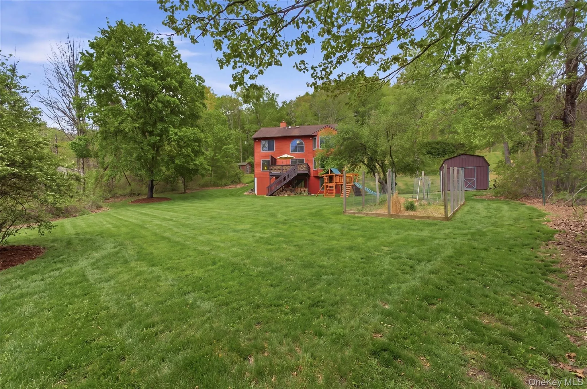 Back of house with expansive green lawn with mature trees, featuring a multi-level deck, a fenced garden area, and an accessory shed. Back of house with expansive green lawn with mature trees, featuring a multi-level deck, a fenced garden area, and an accessory shed.