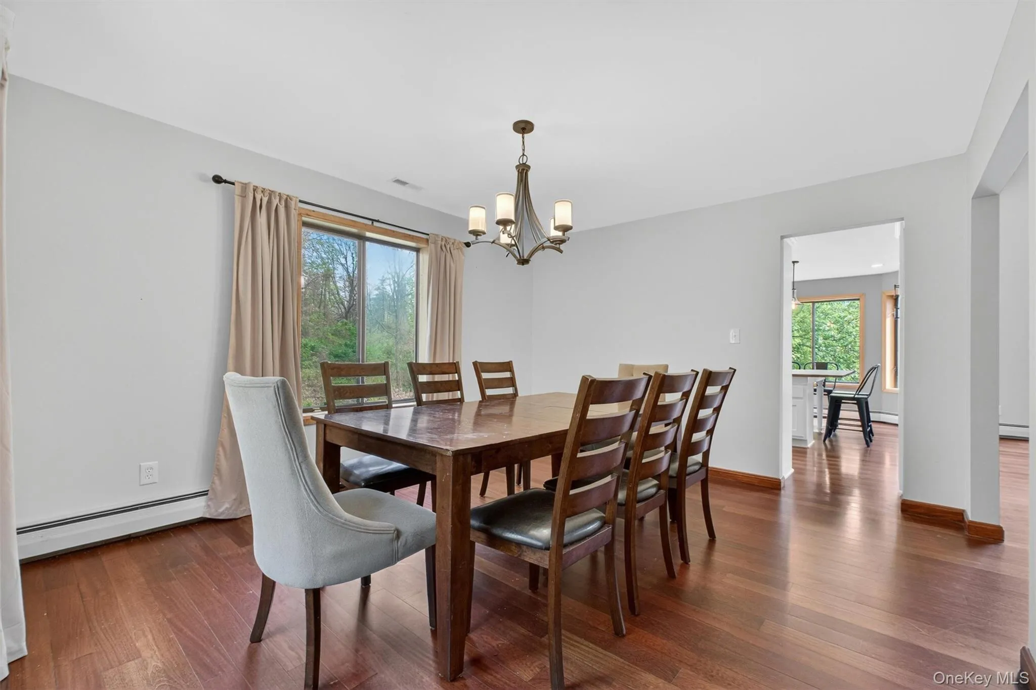 Dining area featuring wood-finish flooring, two large windows, and a chandelier that opens into the kitchen and living rooms. Dining area featuring wood-finish flooring, two large windows, and a chandelier that opens into the kitchen and living rooms.