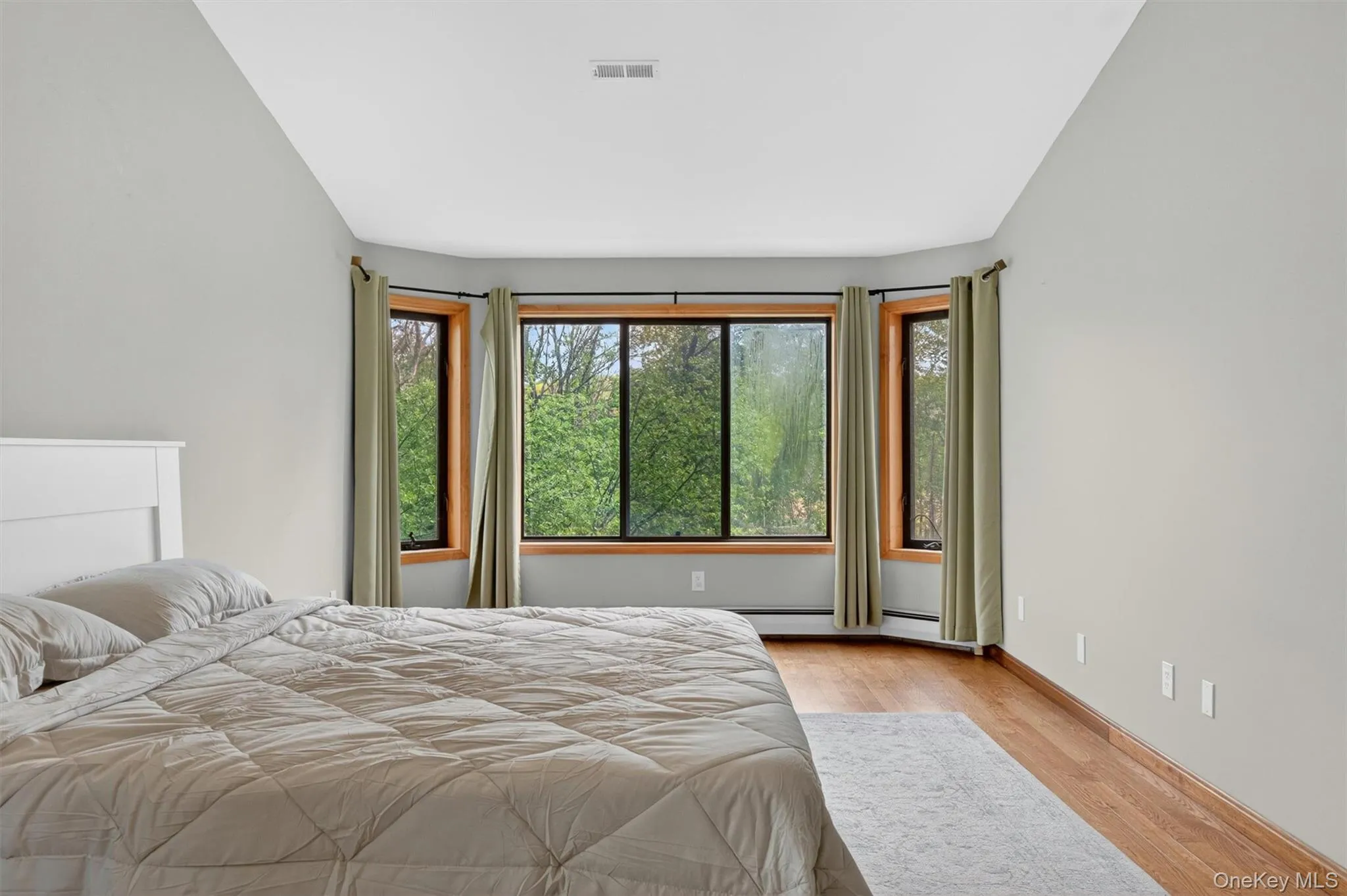 Spacious vaulted ceiling bedroom featuring wood-finish flooring, a ceiling fan, and multiple windows with wood trim Spacious vaulted ceiling bedroom featuring wood-finish flooring, a ceiling fan, and multiple windows with wood trim