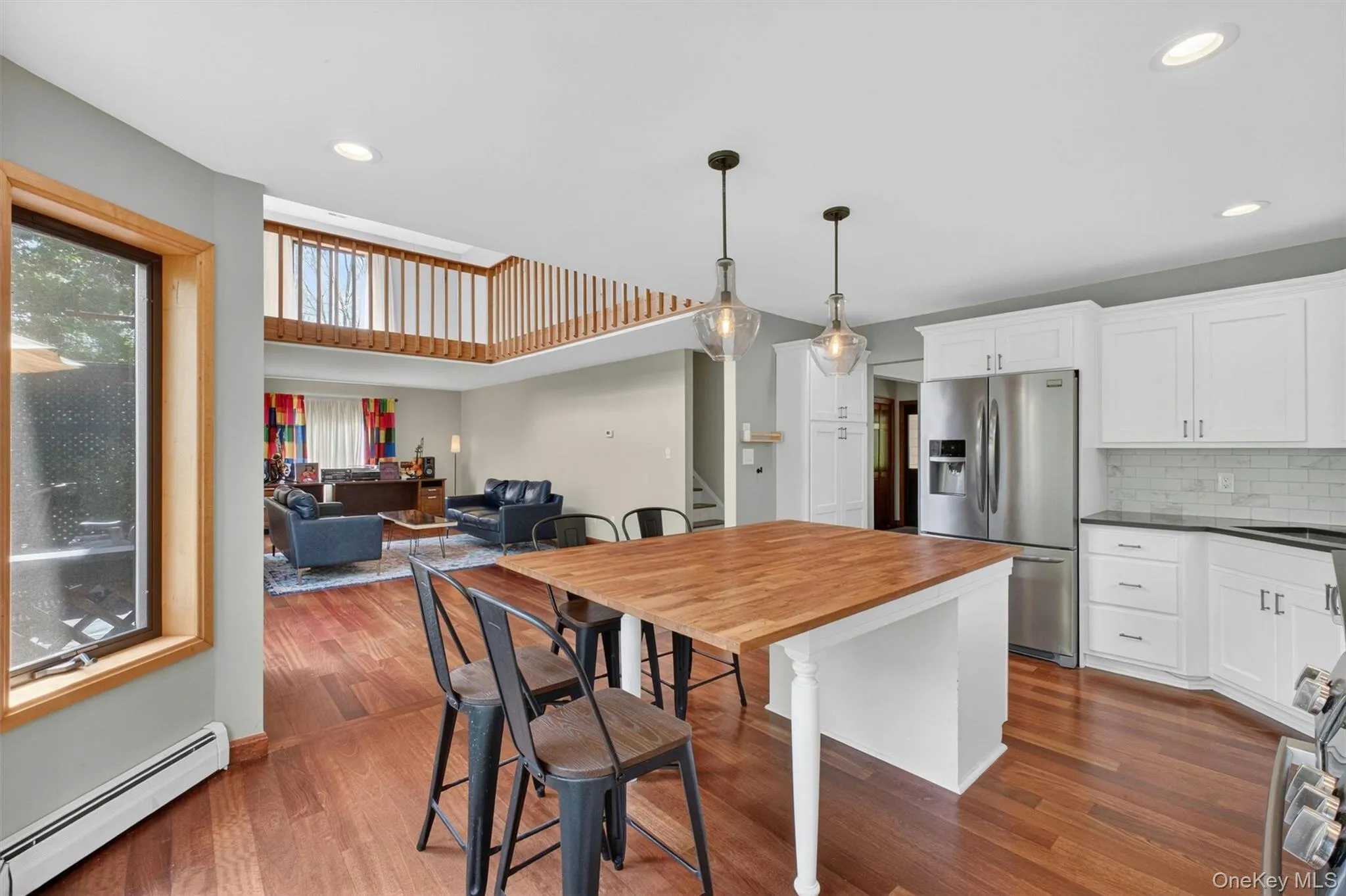 Open-concept kitchen featuring an island with butcher block countertop, white cabinetry, stainless steel appliances, and wood-finish flooring leading to the open living room. Open-concept kitchen featuring an island with butcher block countertop, white cabinetry, stainless steel appliances, and wood-finish flooring leading to the open living room.