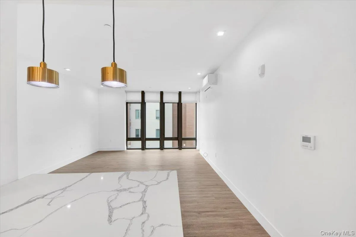 Open-concept interior featuring large windows, wood-finish flooring, recessed lighting, and a white countertop with grey veining Open-concept interior featuring large windows, wood-finish flooring, recessed lighting, and a white countertop with grey veining