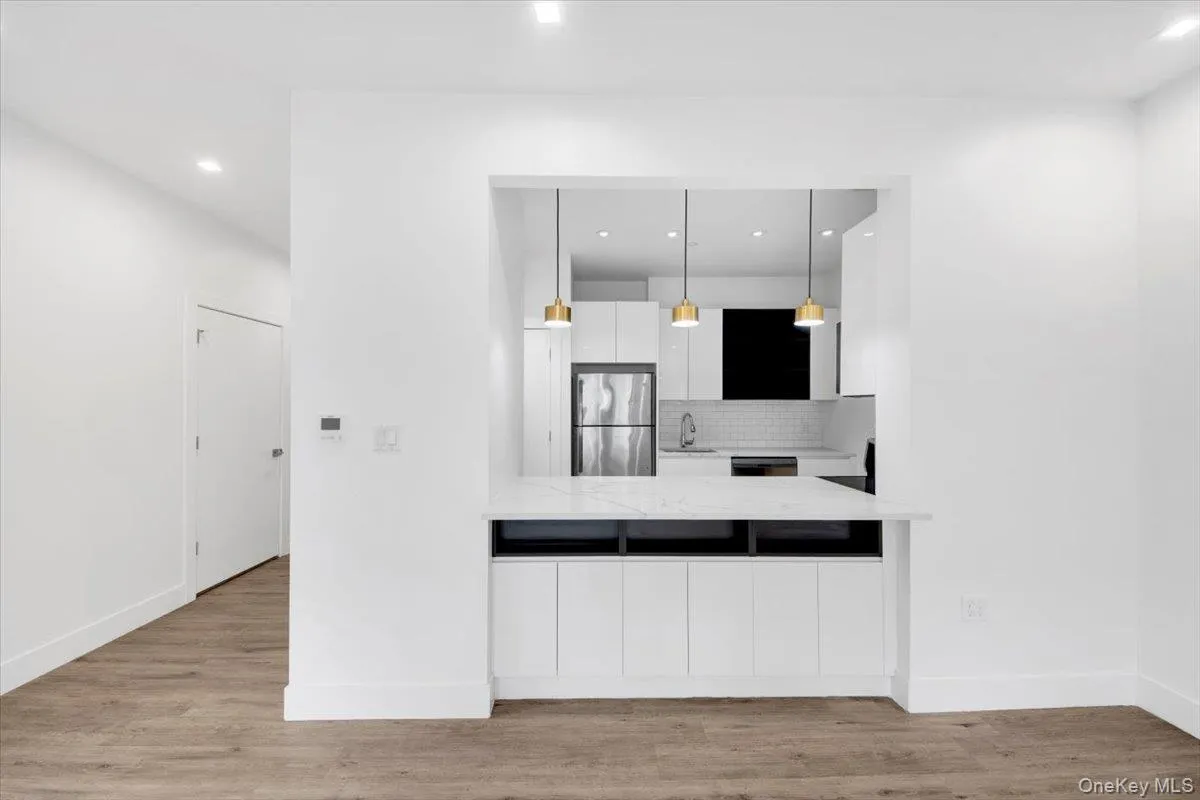Contemporary kitchen passthrough featuring a white countertop, recessed lighting, and wood-finish flooring Contemporary kitchen passthrough featuring a white countertop, recessed lighting, and wood-finish flooring