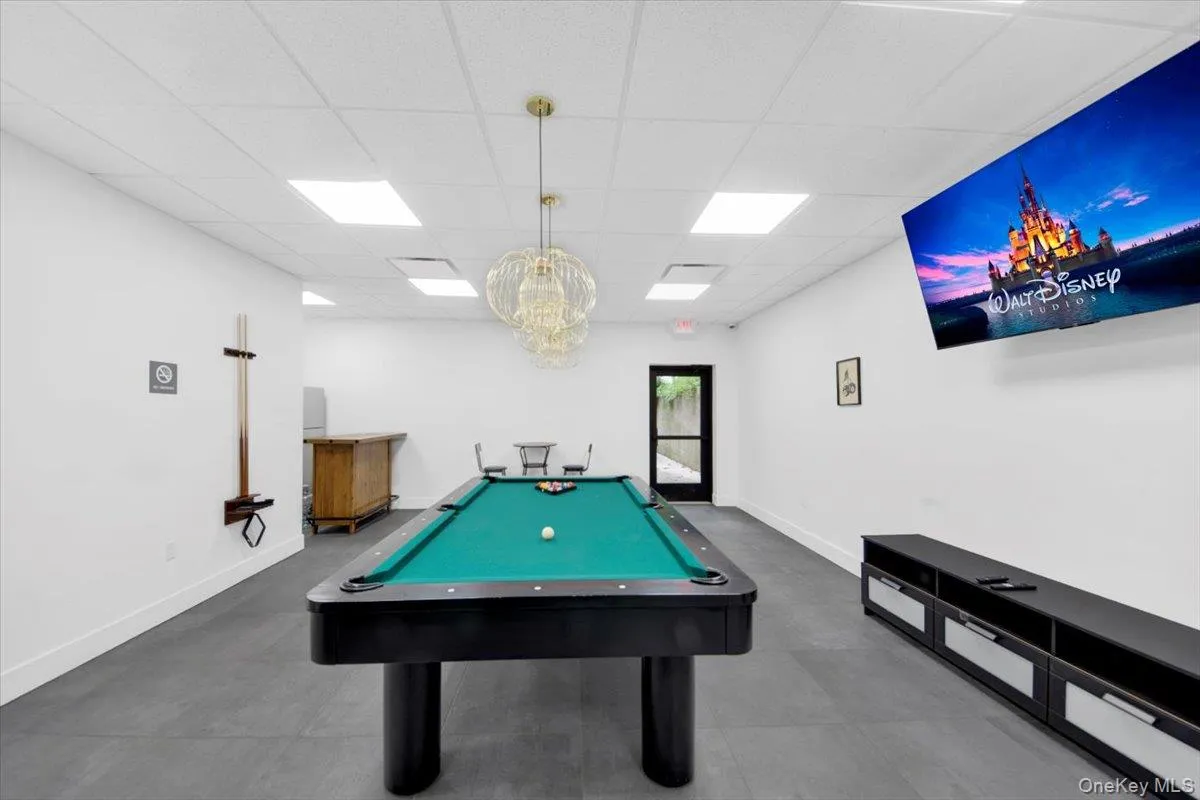 Recreation room featuring a pool table with a green felt surface and dark wood finish, modern overhead lighting, and a wall-mounted display Recreation room featuring a pool table with a green felt surface and dark wood finish, modern overhead lighting, and a wall-mounted display