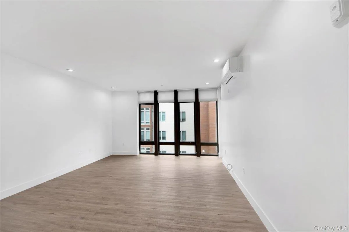 Spacious room featuring wood-finish flooring, white walls, and recessed lighting Spacious room featuring wood-finish flooring, white walls, and recessed lighting