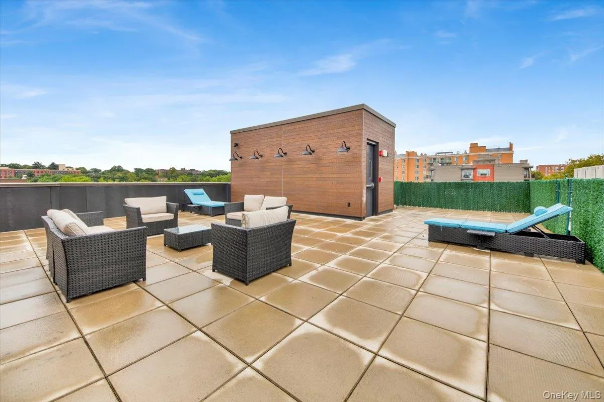 Spacious rooftop terrace featuring large format paver flooring, a wood-paneled utility structure with exterior lighting, and a perimeter privacy screen Spacious rooftop terrace featuring large format paver flooring, a wood-paneled utility structure with exterior lighting, and a perimeter privacy screen