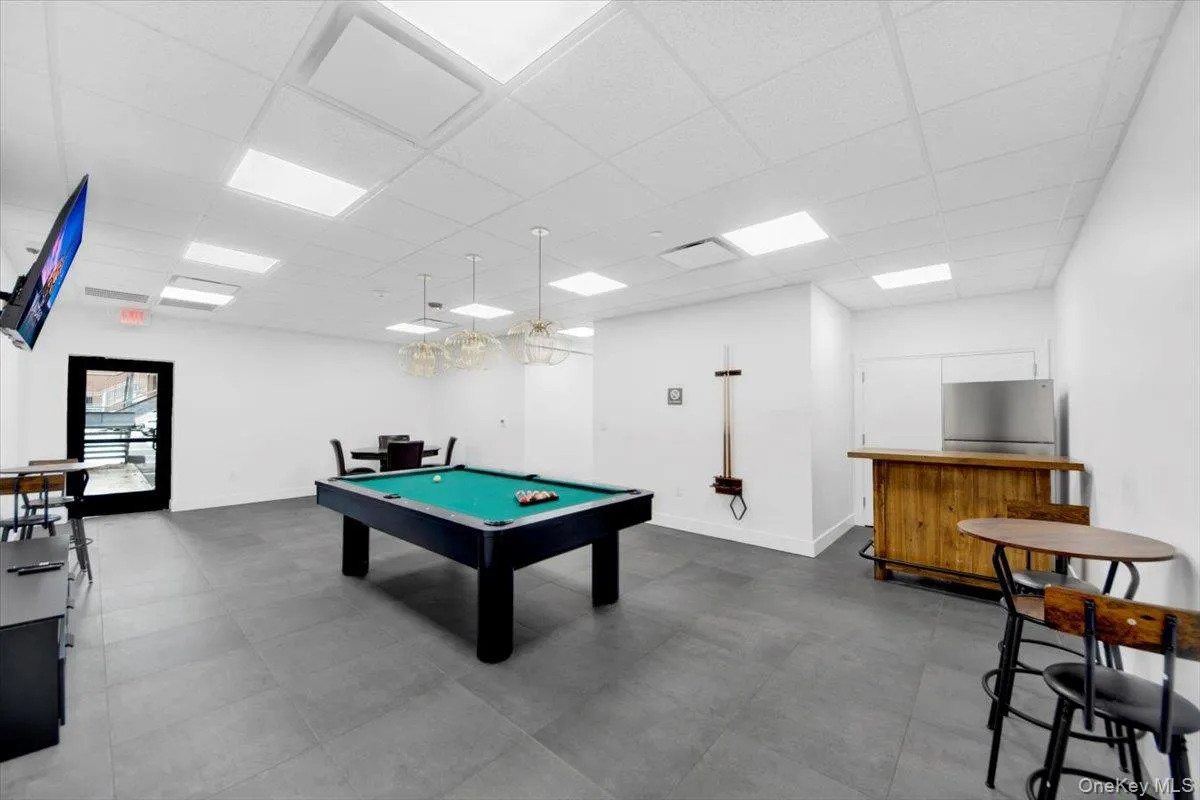Spacious recreation area featuring a pool table, gray tile flooring, recessed panel lighting, and modern pendant light fixtures Spacious recreation area featuring a pool table, gray tile flooring, recessed panel lighting, and modern pendant light fixtures