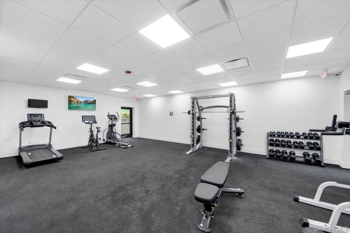 Fitness room featuring dark rubber flooring, recessed lighting, white walls, and a variety of exercise equipment Fitness room featuring dark rubber flooring, recessed lighting, white walls, and a variety of exercise equipment