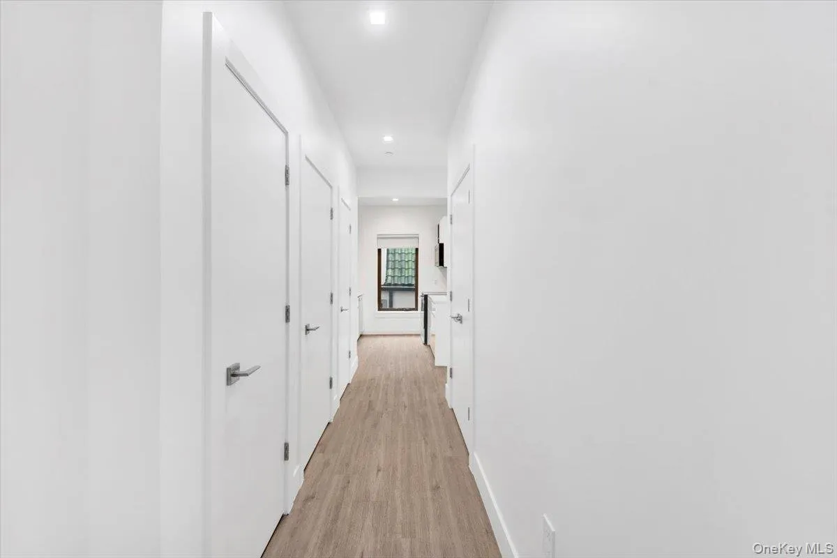 Hallway featuring wood-finish flooring, white walls, flush-mounted ceiling lights, and contemporary interior doors with satin nickel hardware Hallway featuring wood-finish flooring, white walls, flush-mounted ceiling lights, and contemporary interior doors with satin nickel hardware