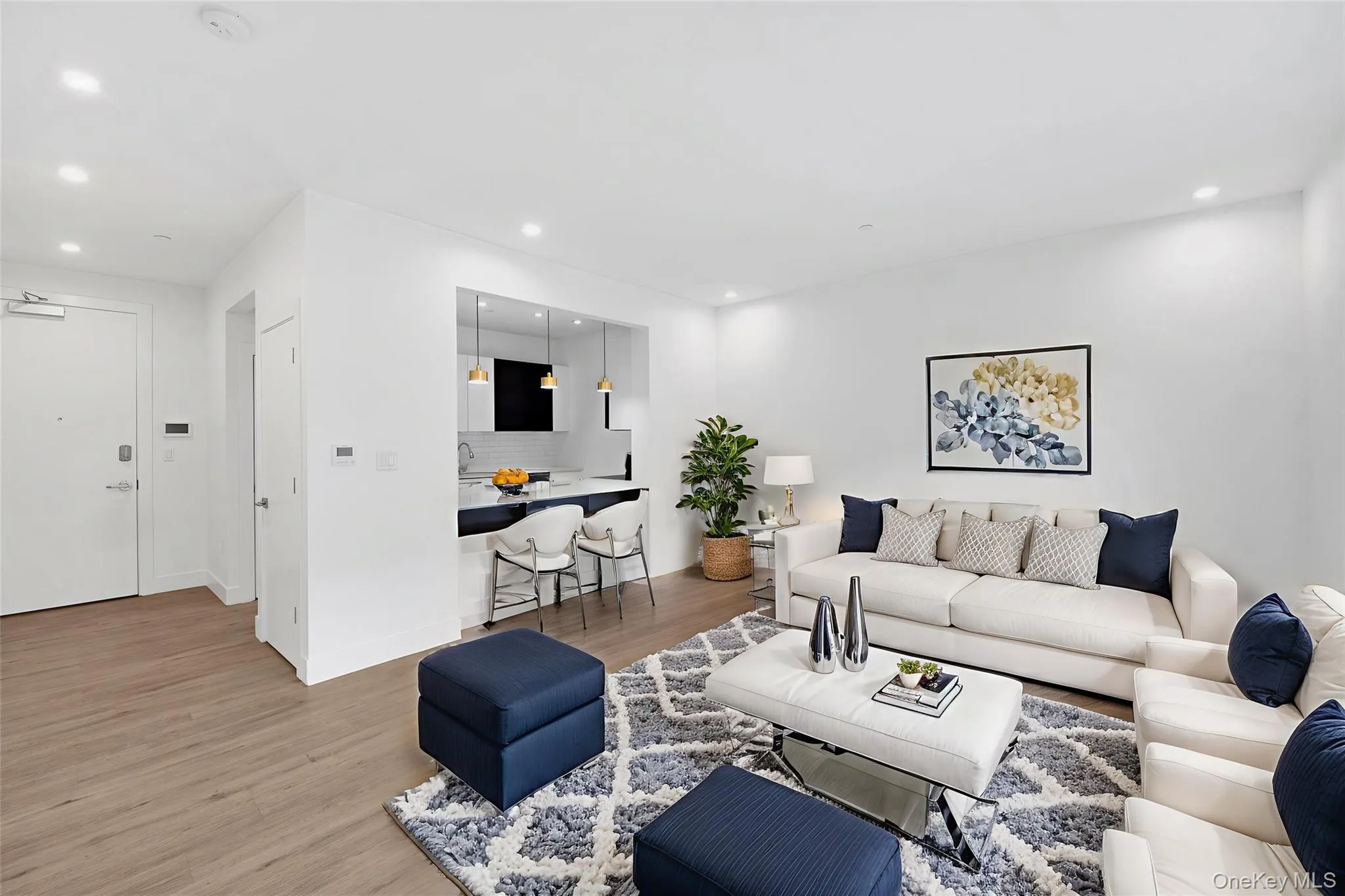 Open-concept living area featuring wood-finish flooring, recessed lighting, and a kitchen pass-through with pendant lighting Open-concept living area featuring wood-finish flooring, recessed lighting, and a kitchen pass-through with pendant lighting