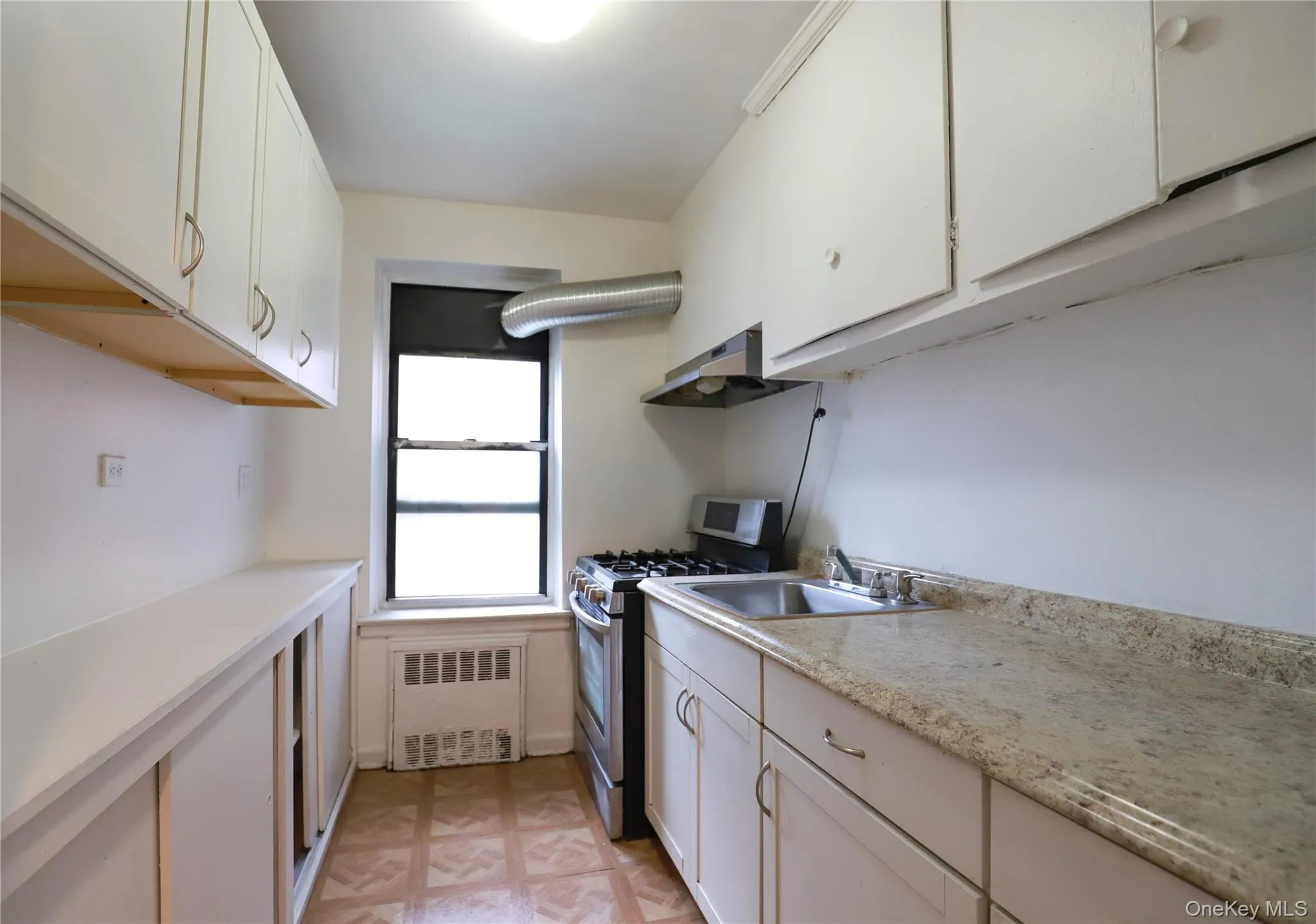Galley kitchen featuring a window, wood-finish flooring, white cabinetry, laminate countertops, and a stainless steel oven/range Galley kitchen featuring a window, wood-finish flooring, white cabinetry, laminate countertops, and a stainless steel oven/range