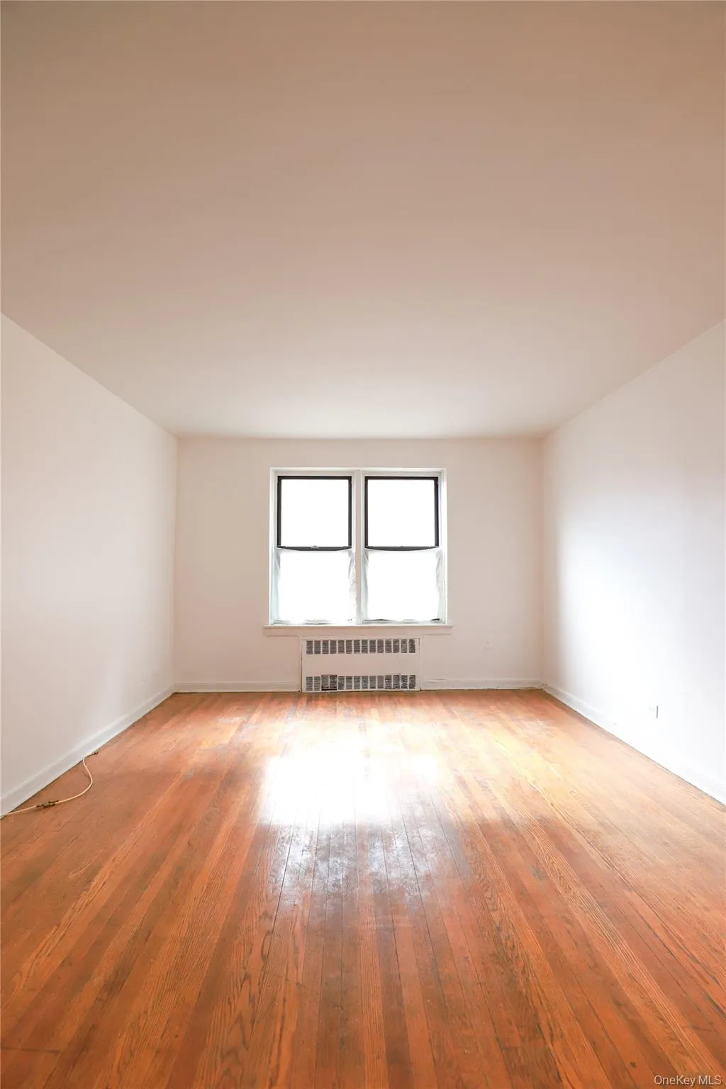 Bright interior space featuring wood-finish flooring, white walls, two windows, and a baseboard radiator Bright interior space featuring wood-finish flooring, white walls, two windows, and a baseboard radiator